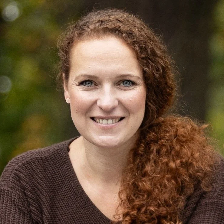 Porträt einer lachenden Frau mit roten, lockigen Haaren vor einer natürlichen Hintergrund
