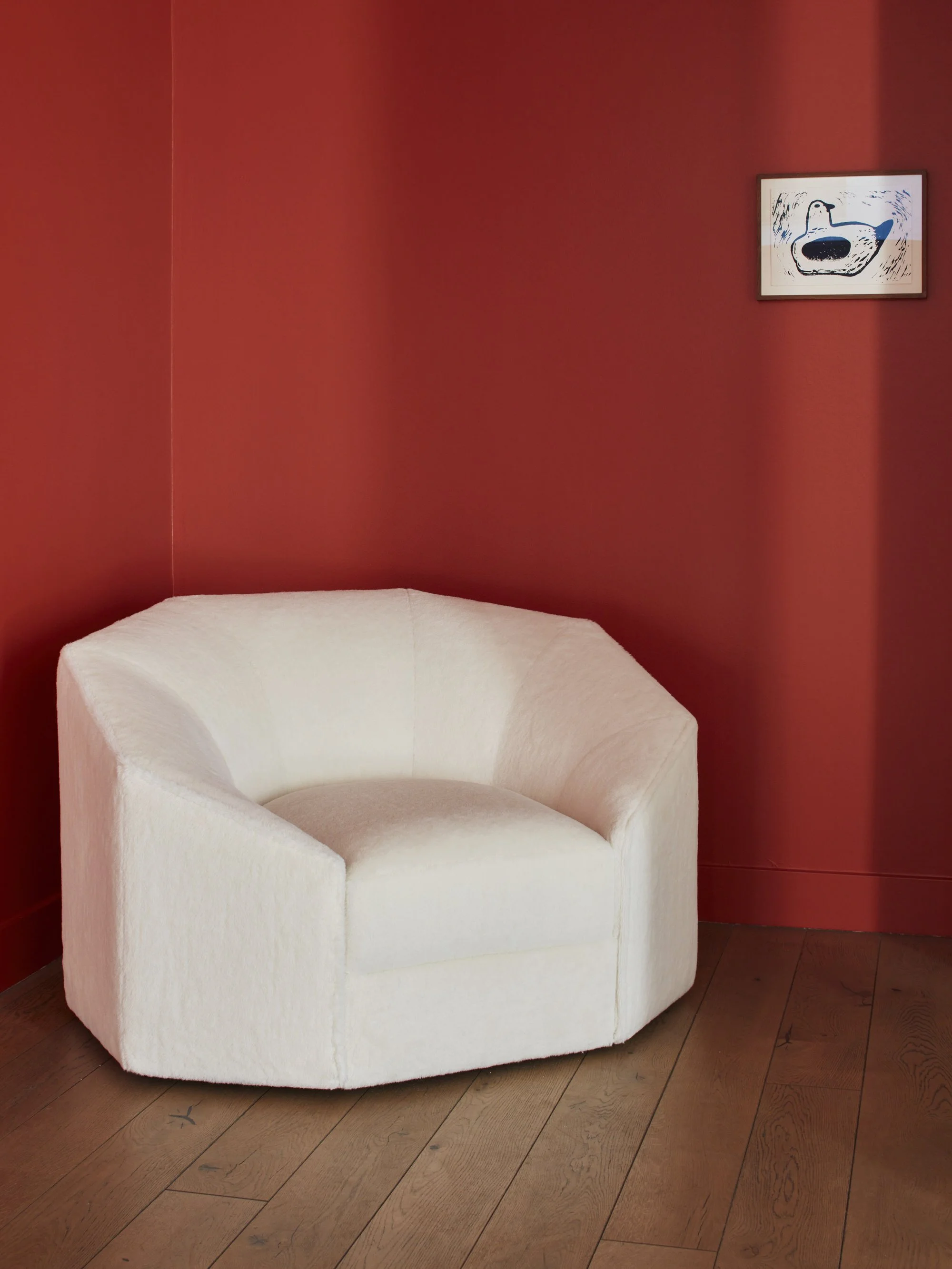 Coin d'une pièce avec un fauteuil blanc en forme d'arc et un tableau abstrait sur le mur rouge.