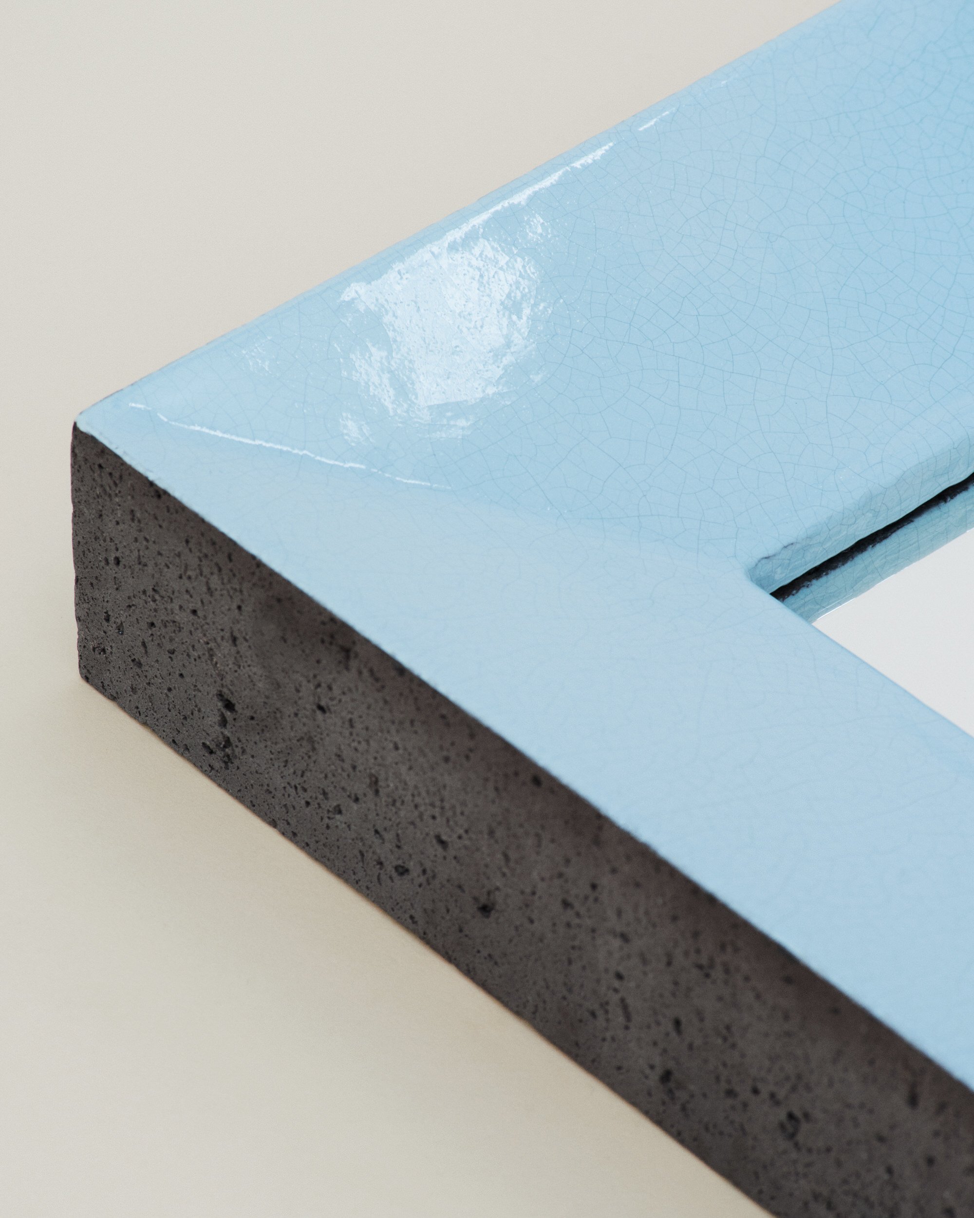 Zoom sur l'angle d'un miroir peint en bleu clair, montée sur un mur blanc.