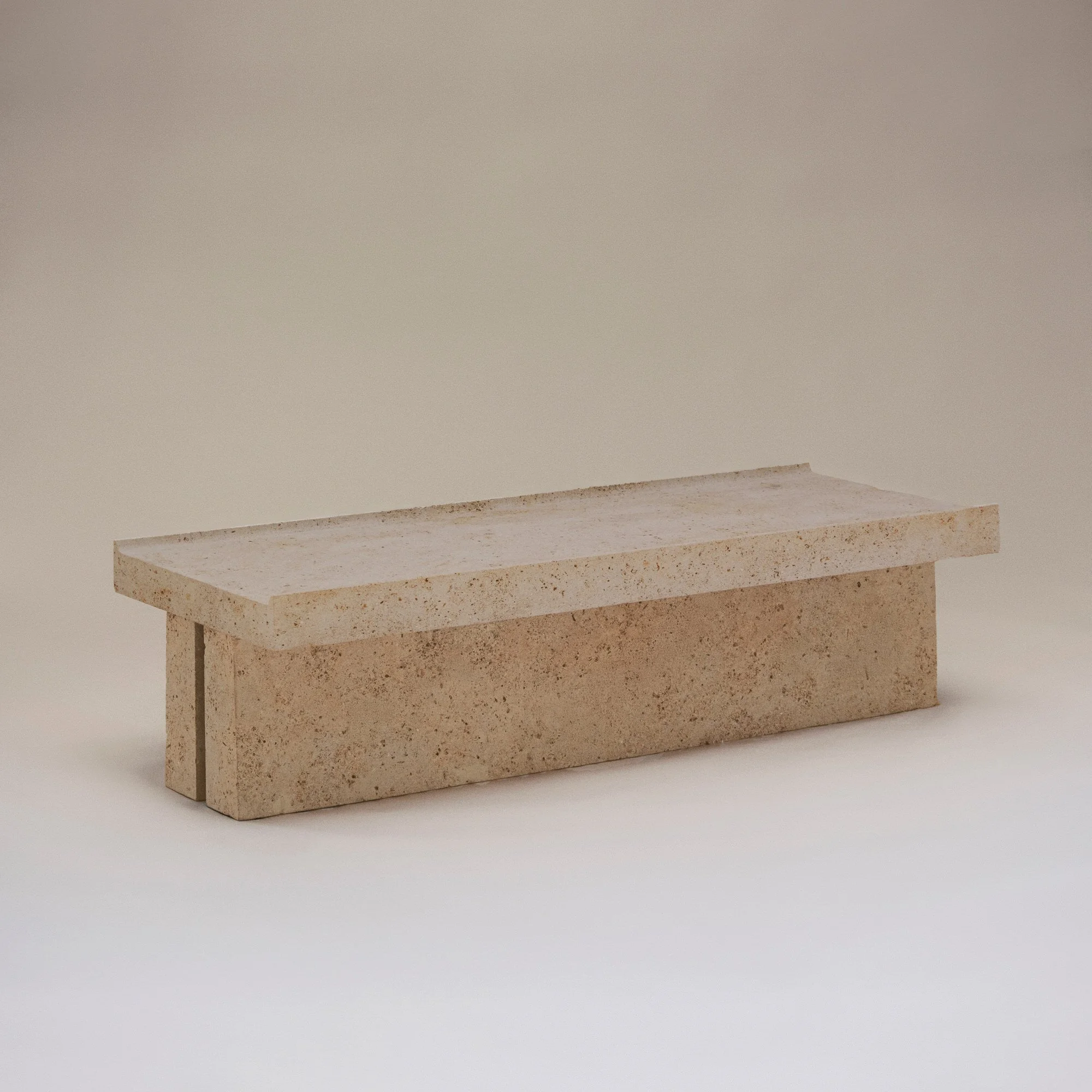 Une petite table en béton de forme rectangulaire avec un plateau épais et une base solide, couleur beige clair, sur un fond neutre.
