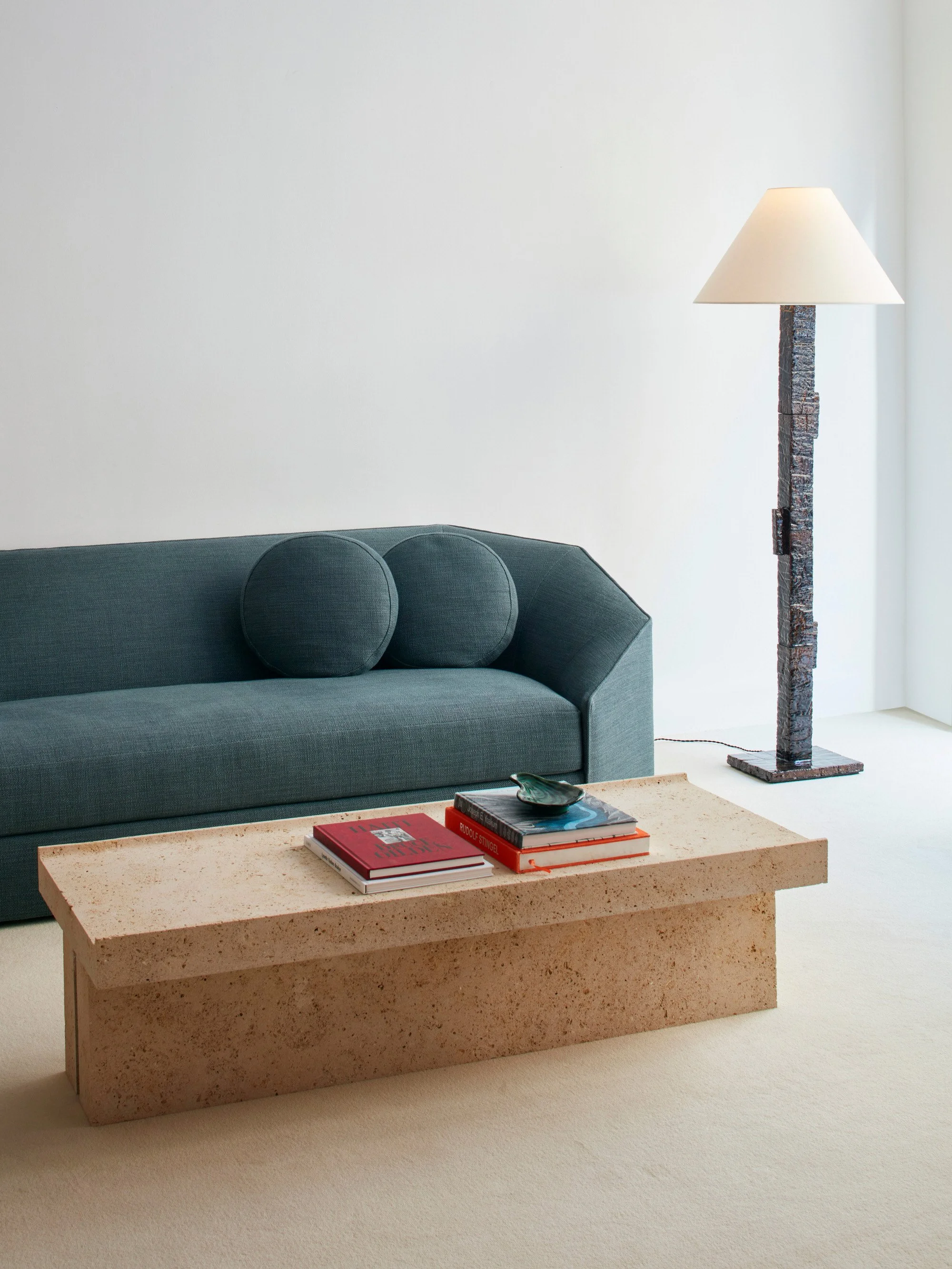 Salon moderne avec un canapé gris, une table en pierre, une lampe de sol et quelques livres sur la table.