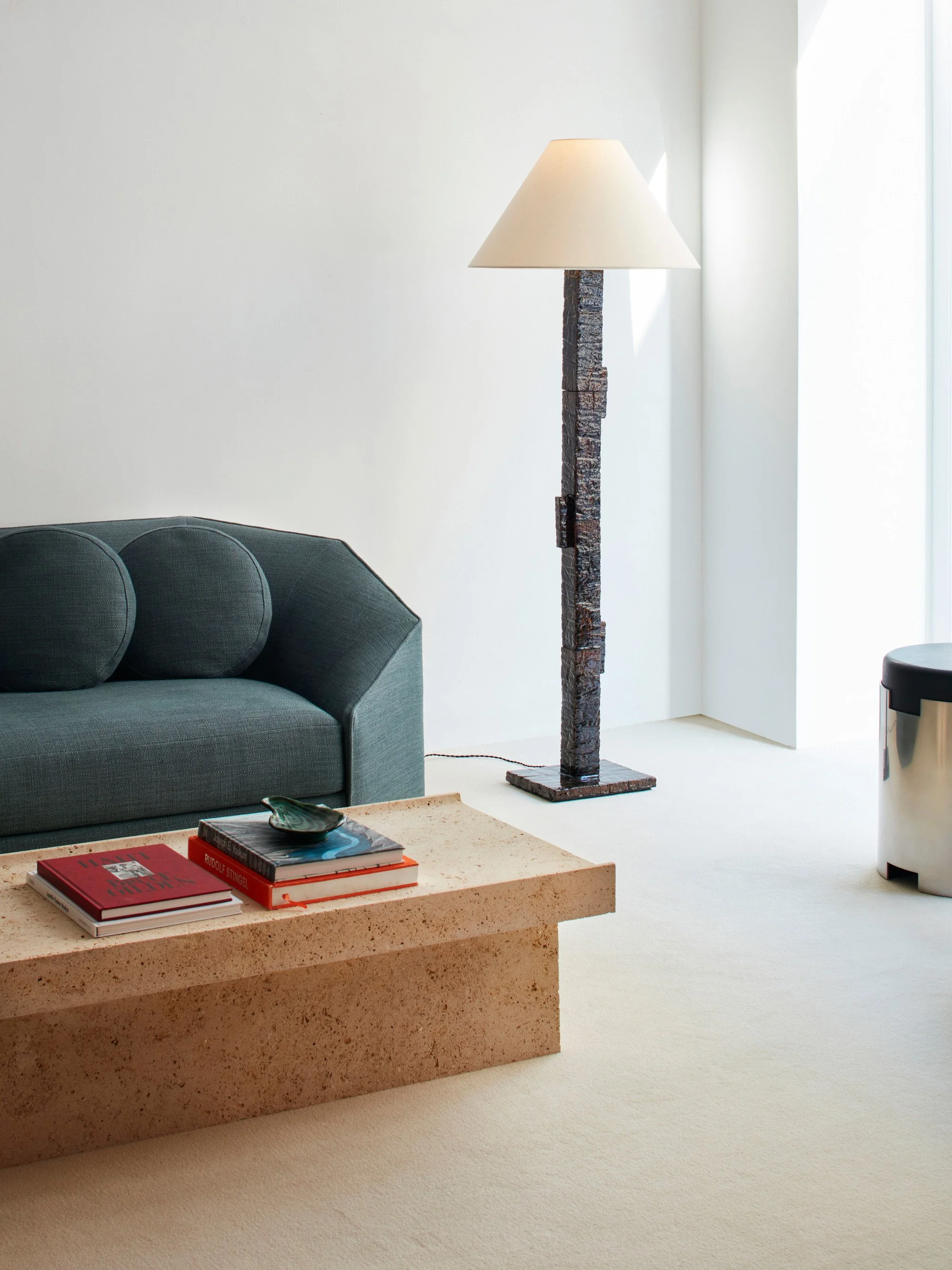 Salon moderne avec un canapé gris, une table basse en pierre, un lampadaire en pierre avec un abat-jour blanc, et une grande fenêtre lumineuse.