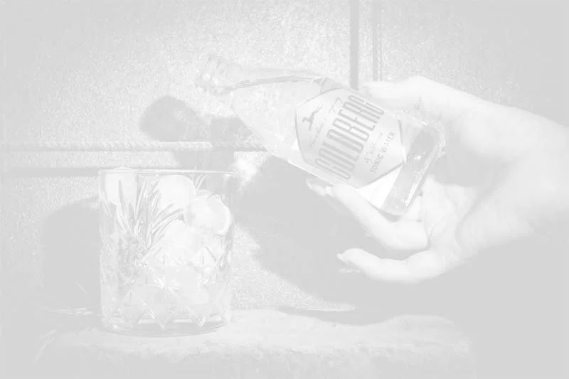 Hand die eine Flasche Goldberg Tonic in ein Glas mit Eiswürfeln und Rosmarin gießt
