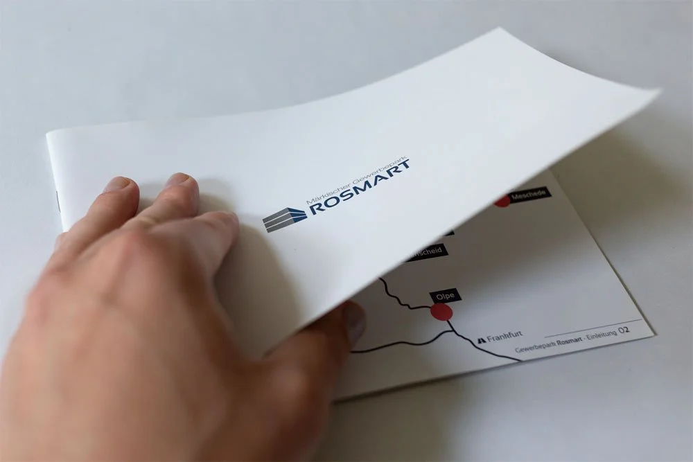 Geschlossene Infobroschüre von Rosmart die grade geöffnet wird.