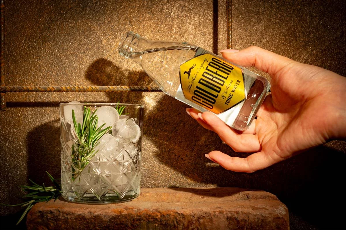 Hand die eine Flasche Goldberg Tonic in ein Glas mit Eiswürfeln schüttet