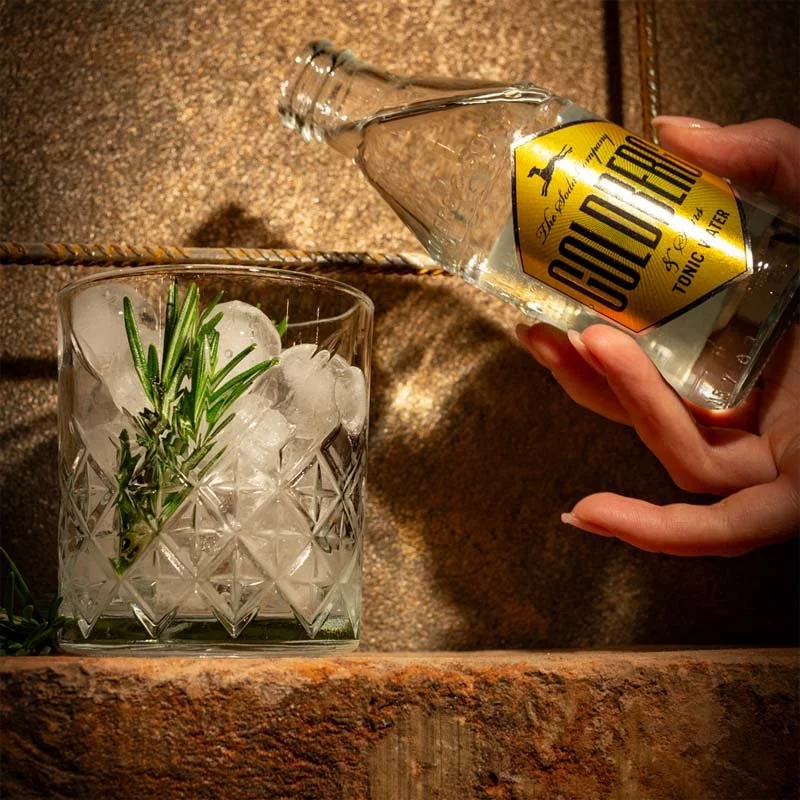 Foto eines Goldbergs Tonic mit einem Glas daneben in dem getrocknete Zitronenscheiben und Eiswürfel liegen
