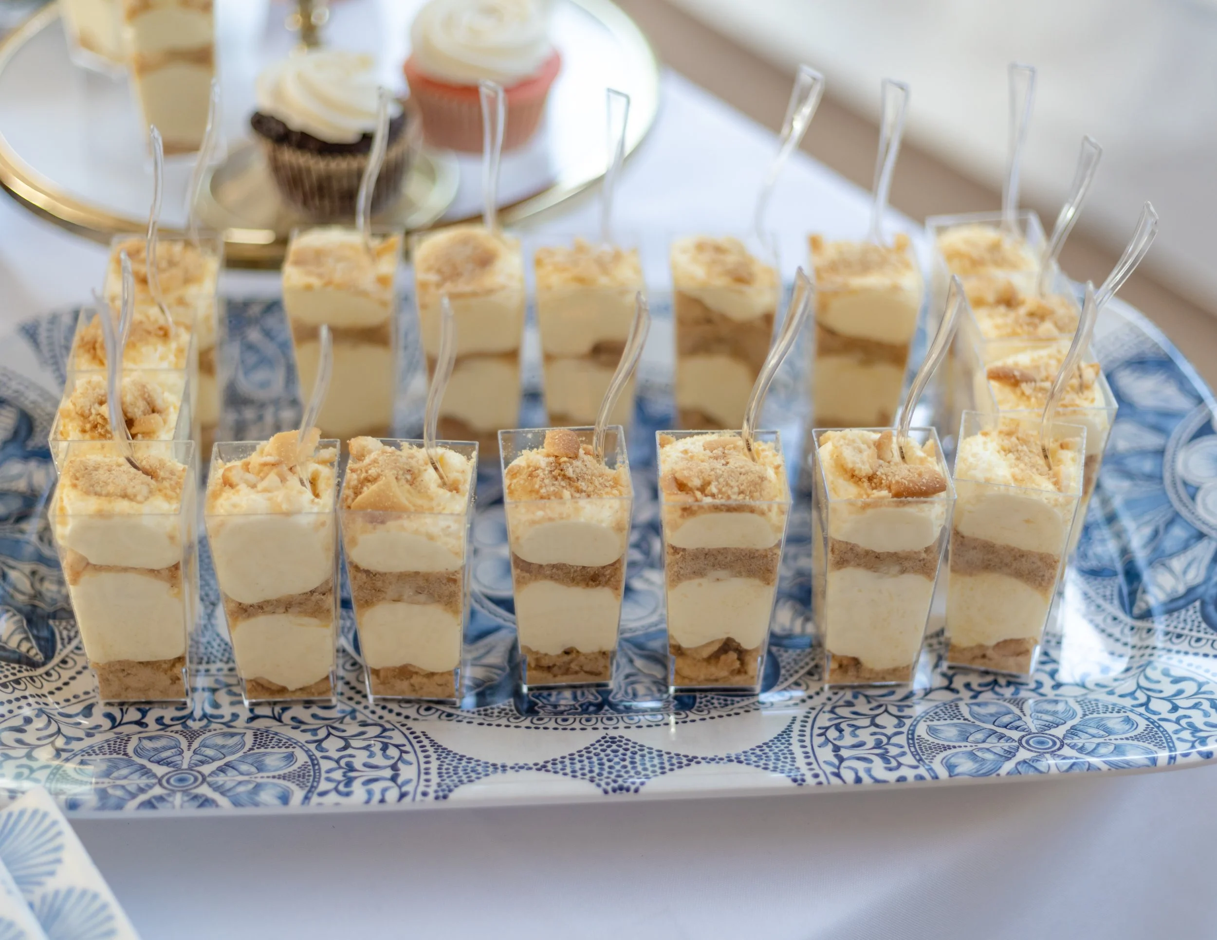 Mini cheesecake desserts topped with crumbs arranged on a silver tray with a blue and white patterned cloth underneath.