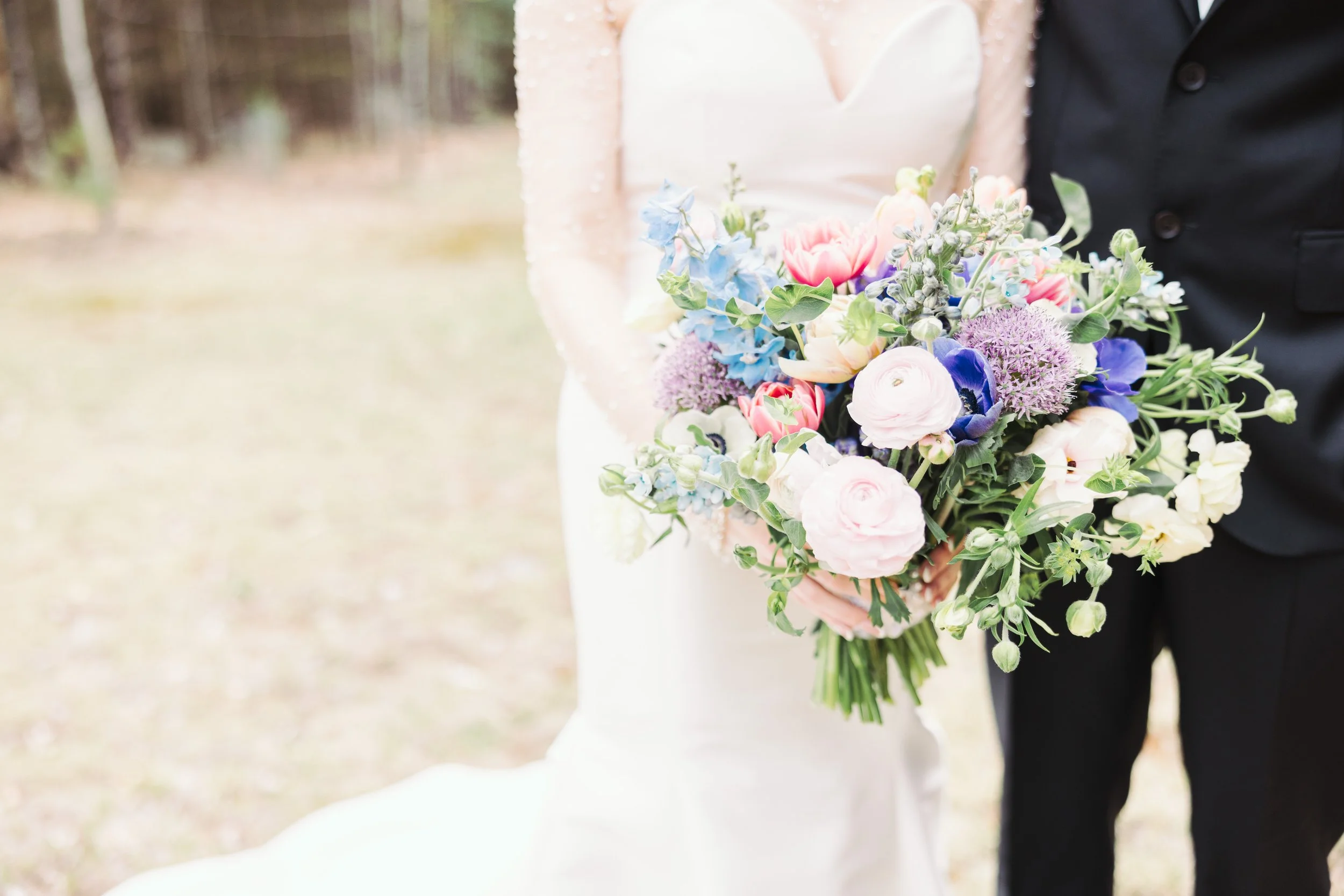 Bride and groom holding a colorful bouquet of flowers outdoors on their wedding day.