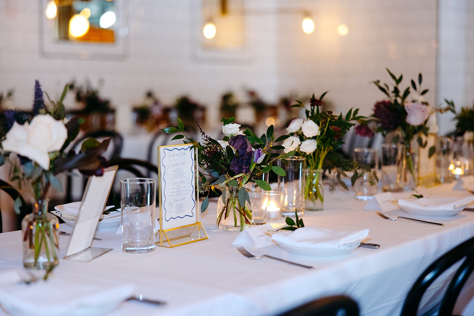 Elegant dining table decorated with floral arrangements, lit candles, glassware, and place settings for a formal event or wedding reception.