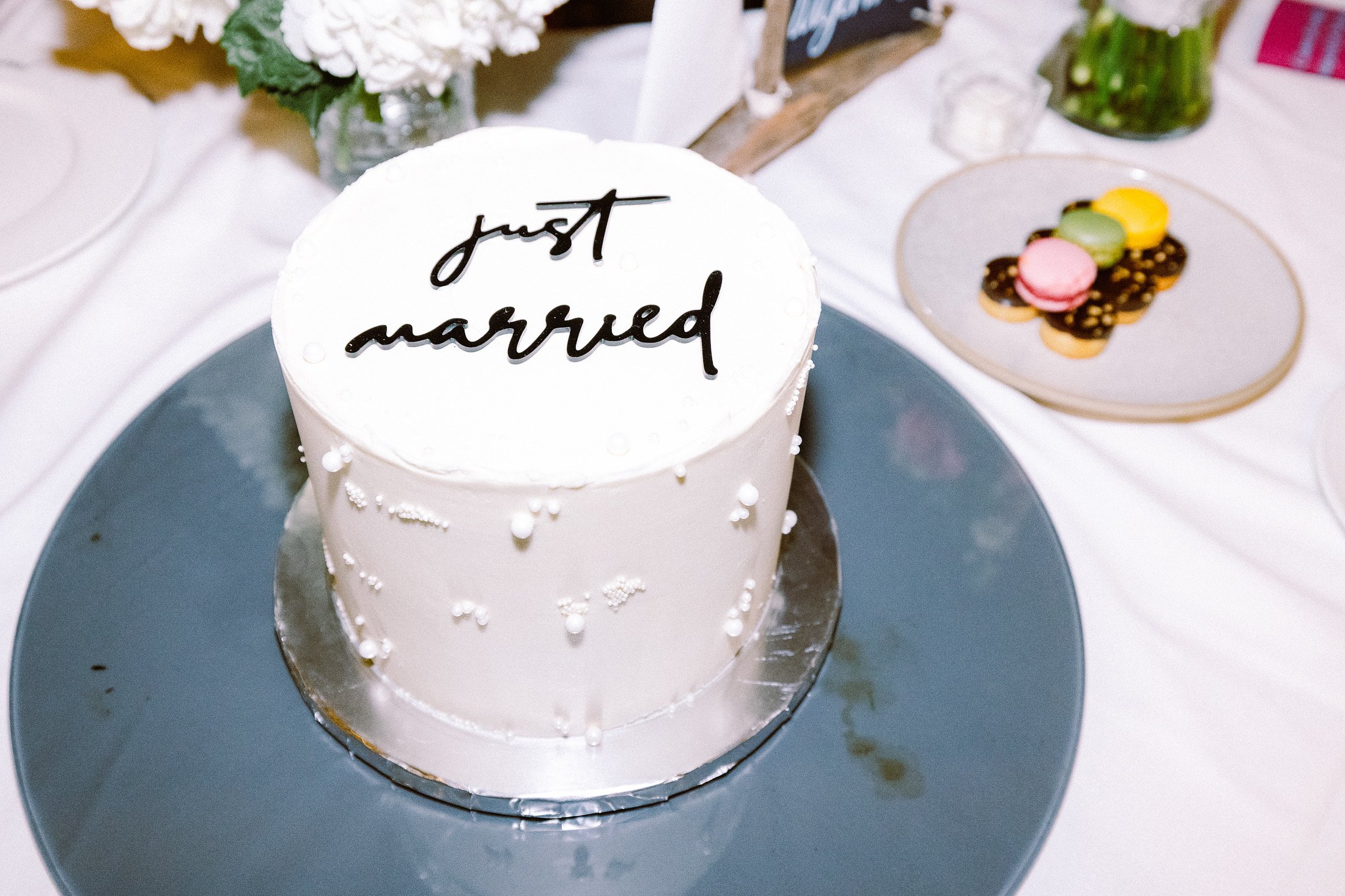A wedding cake with white icing and small white decorative spheres, with the words "just married" written in black on top, placed on a silver cake board.