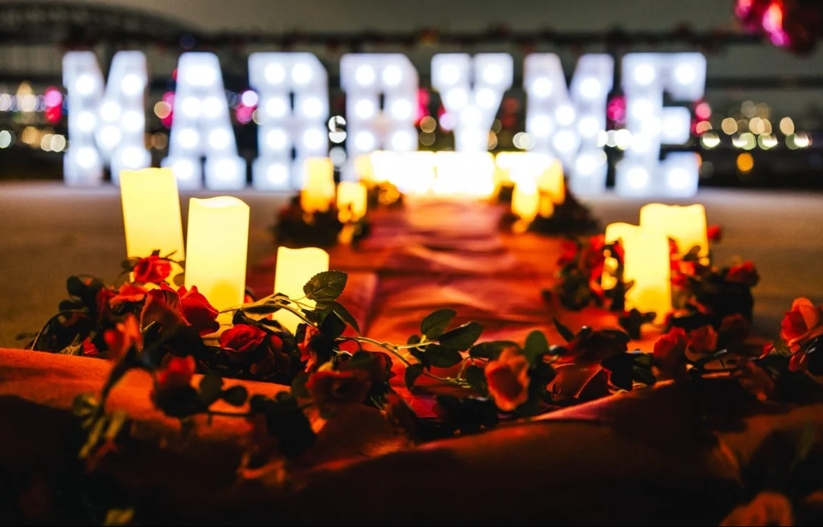 Illuminated 'LOVE' sign in the background with glowing candles and red flowers arranged along a pathway at night.