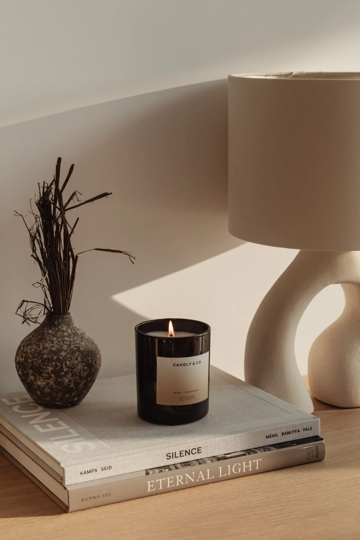 Custom Squarespace Template, E-commerce Squarespace Template, Avelã Creative. A black candle labeled "Candly & Co" sits on top of stacked books titled "Silence" and "Eternal Light," alongside a textured vase with sticks and a modern lamp.