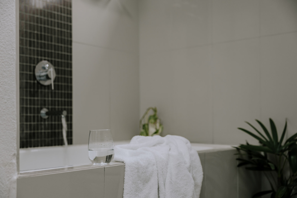 Bathroom with bathtub, a glass of water, a white towel, and a plant.