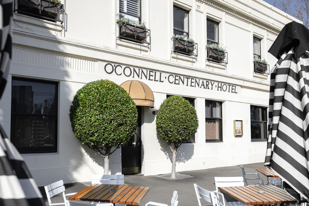 Exterior of the O'Connell Centenary Hotel, South Melbourne, with two trimmed trees in front and outdoor dining tables.
