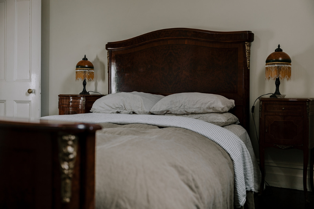 A vintage wooden bed with a dark polished headboard, two nightstands with matching lamps, and a white wall in the background.