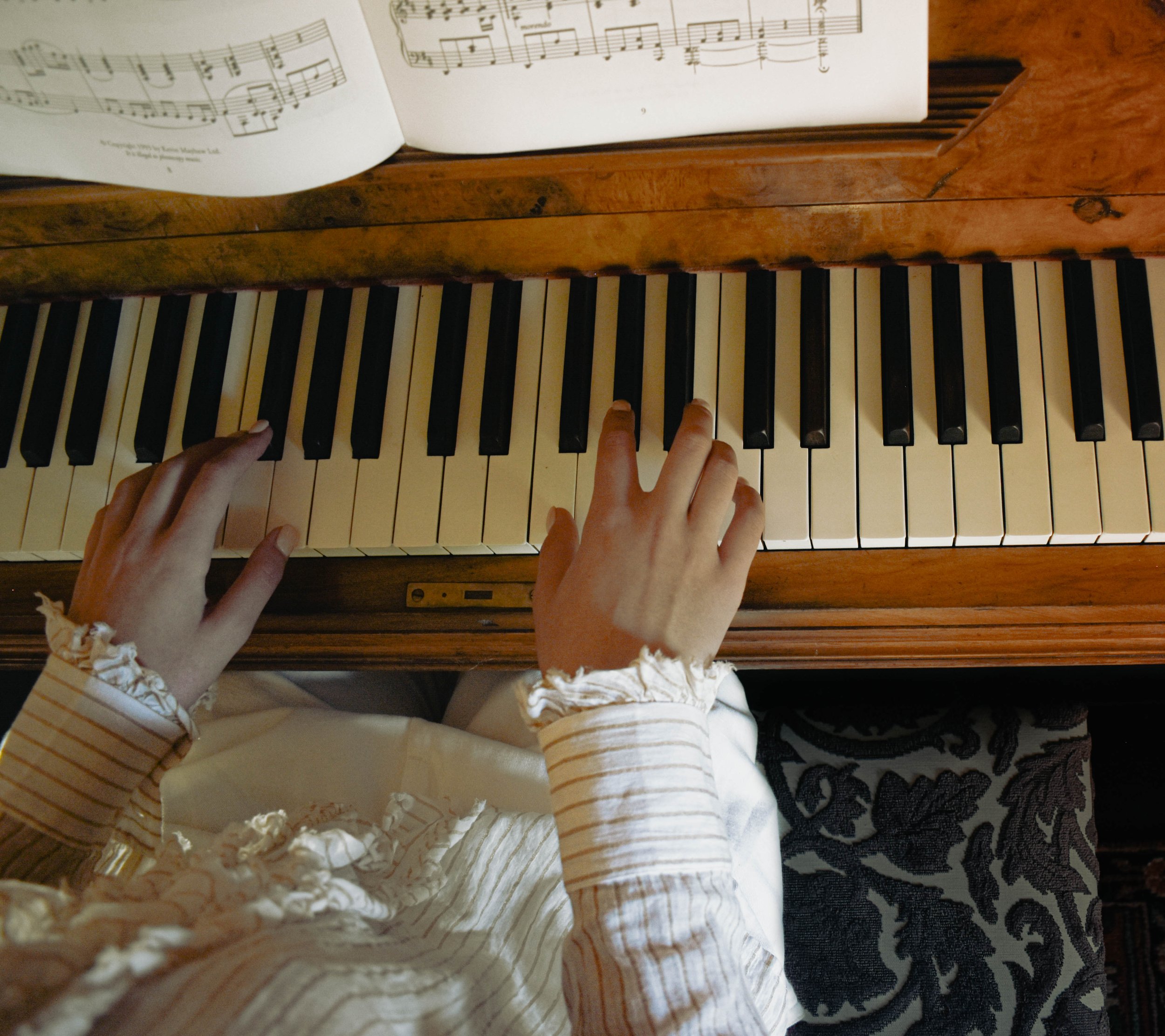 A child's hands playing a traditional wooden piano with sheet music open on top.