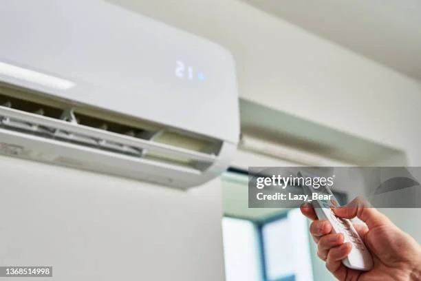 Close-up of a hand holding a remote control pointing at a white wall-mounted air conditioner.