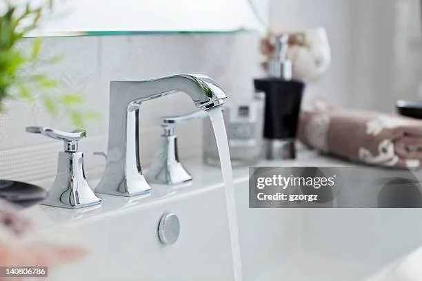 A bathroom sink faucet with water flowing into the sink, surrounded by toiletries and a towel.