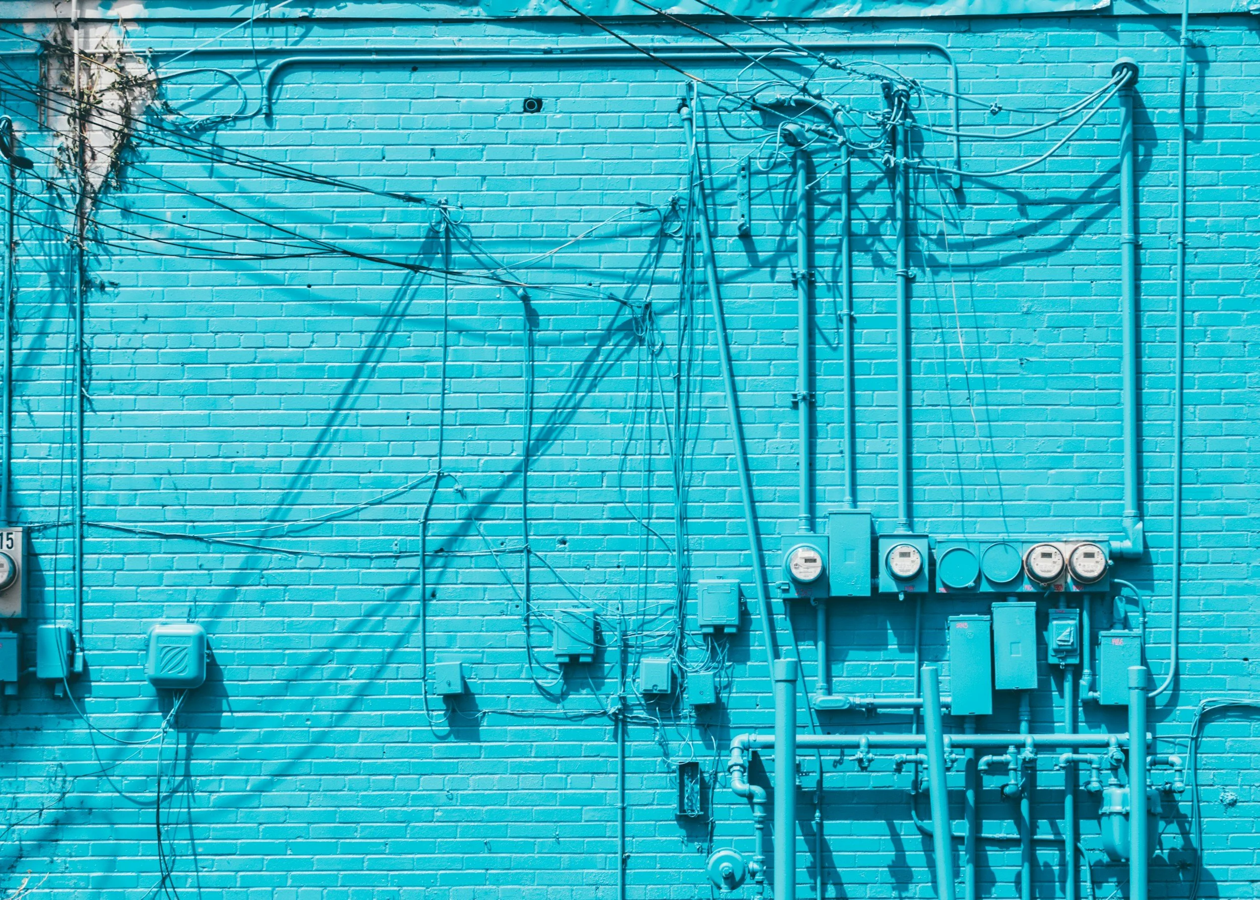 Exterior view of a utility wall with exposed electrical meters, conduits, and service cables, representing energy infrastructure compliance and technical inspection.