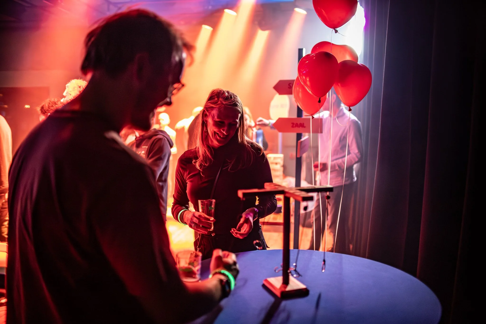 Mensen die samen plezier maken in een donkere ruimte met fel gekleurde lichten, ballonnen en linten.