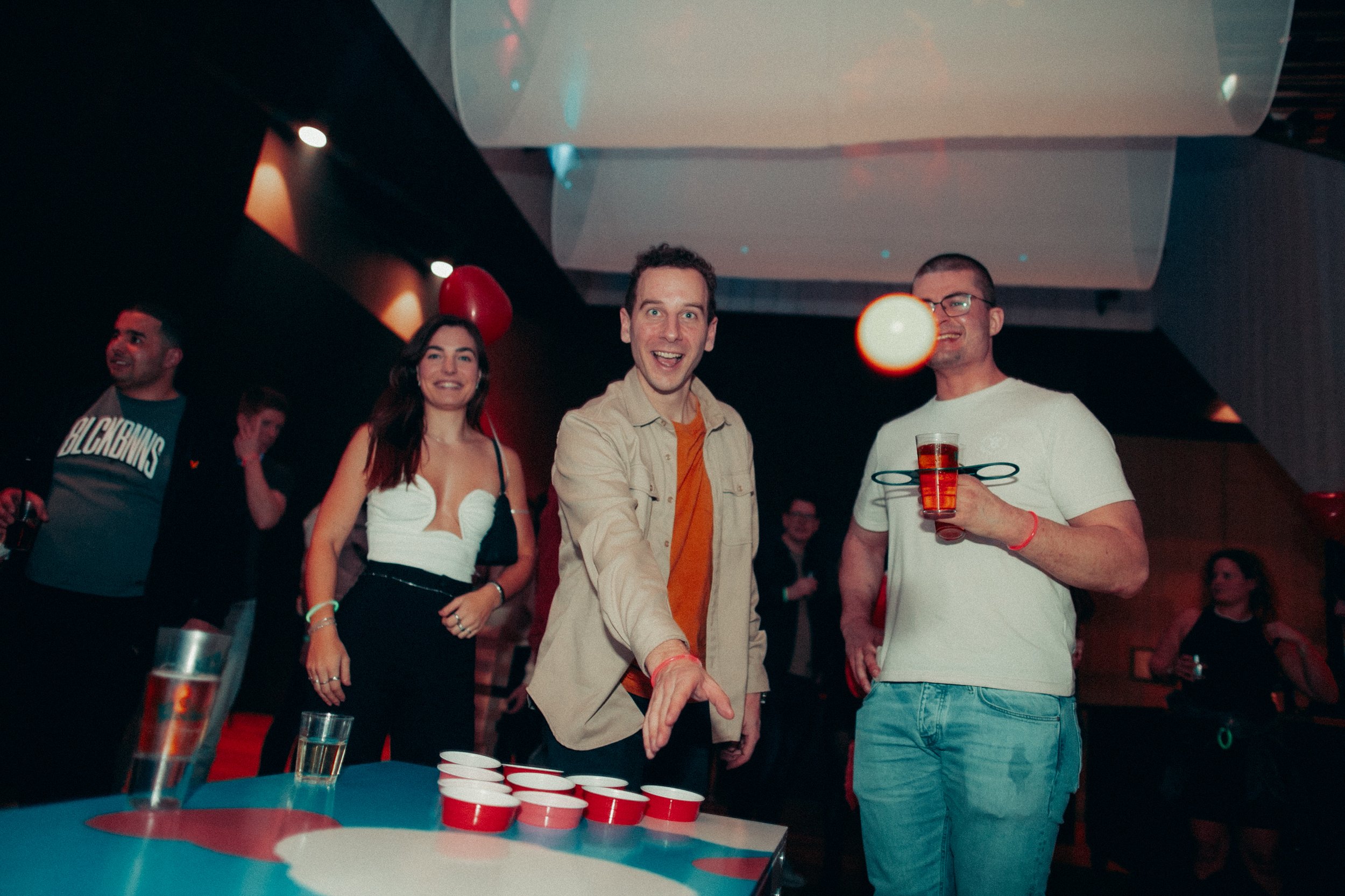 People playing beer pong at a party with drinks and smiles.