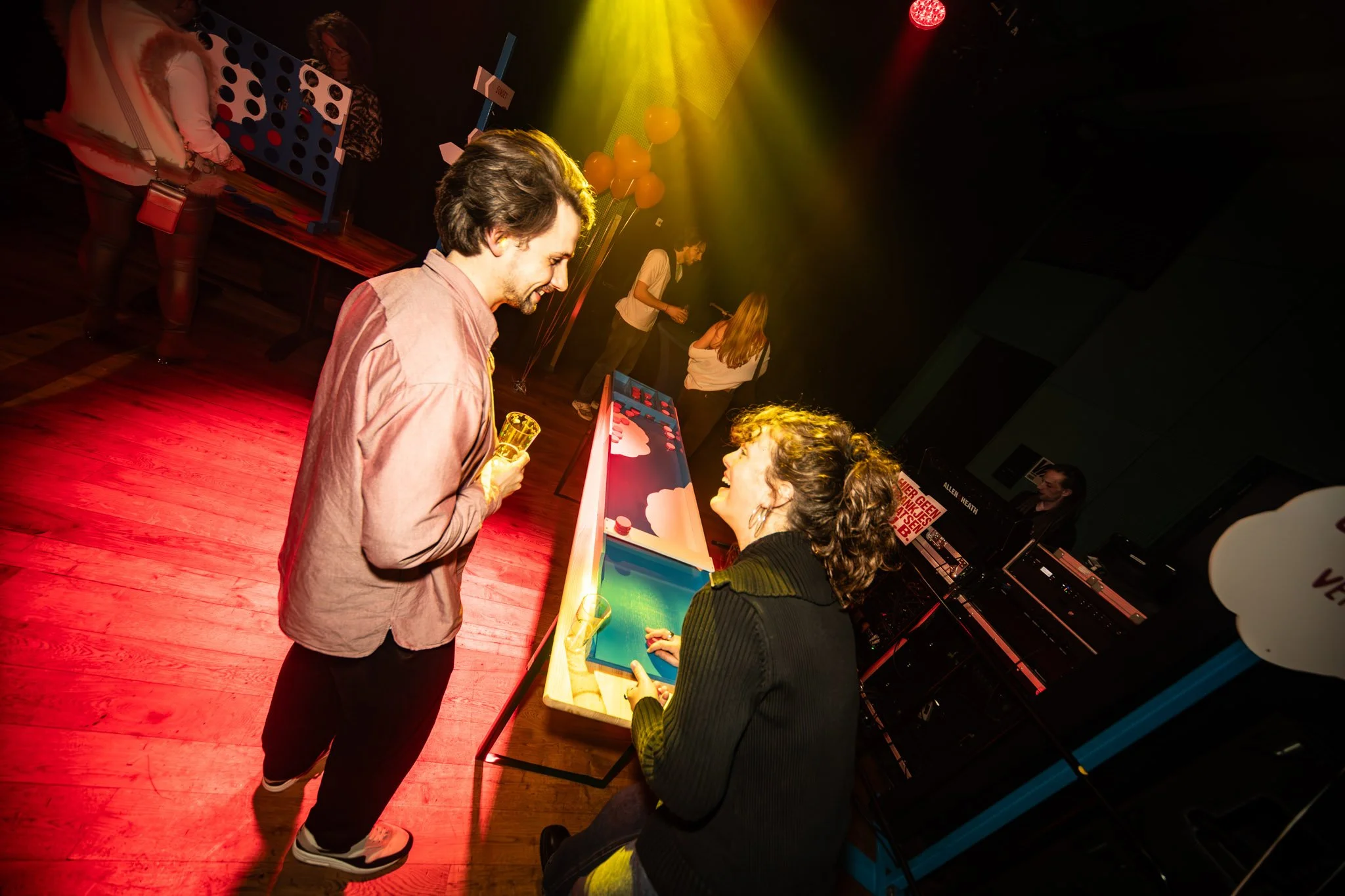 Mensen spelen een Arcade-spel samen in een donkere ruimte met gekleurde verlichting.