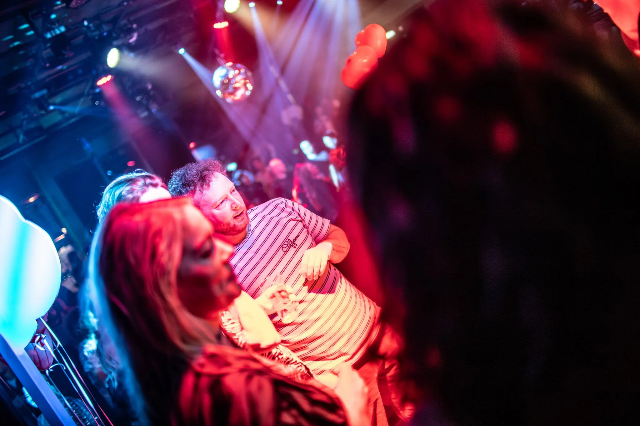 Groep mensen die naar een podium kijken in een discotheek met kleurrijke lichten.