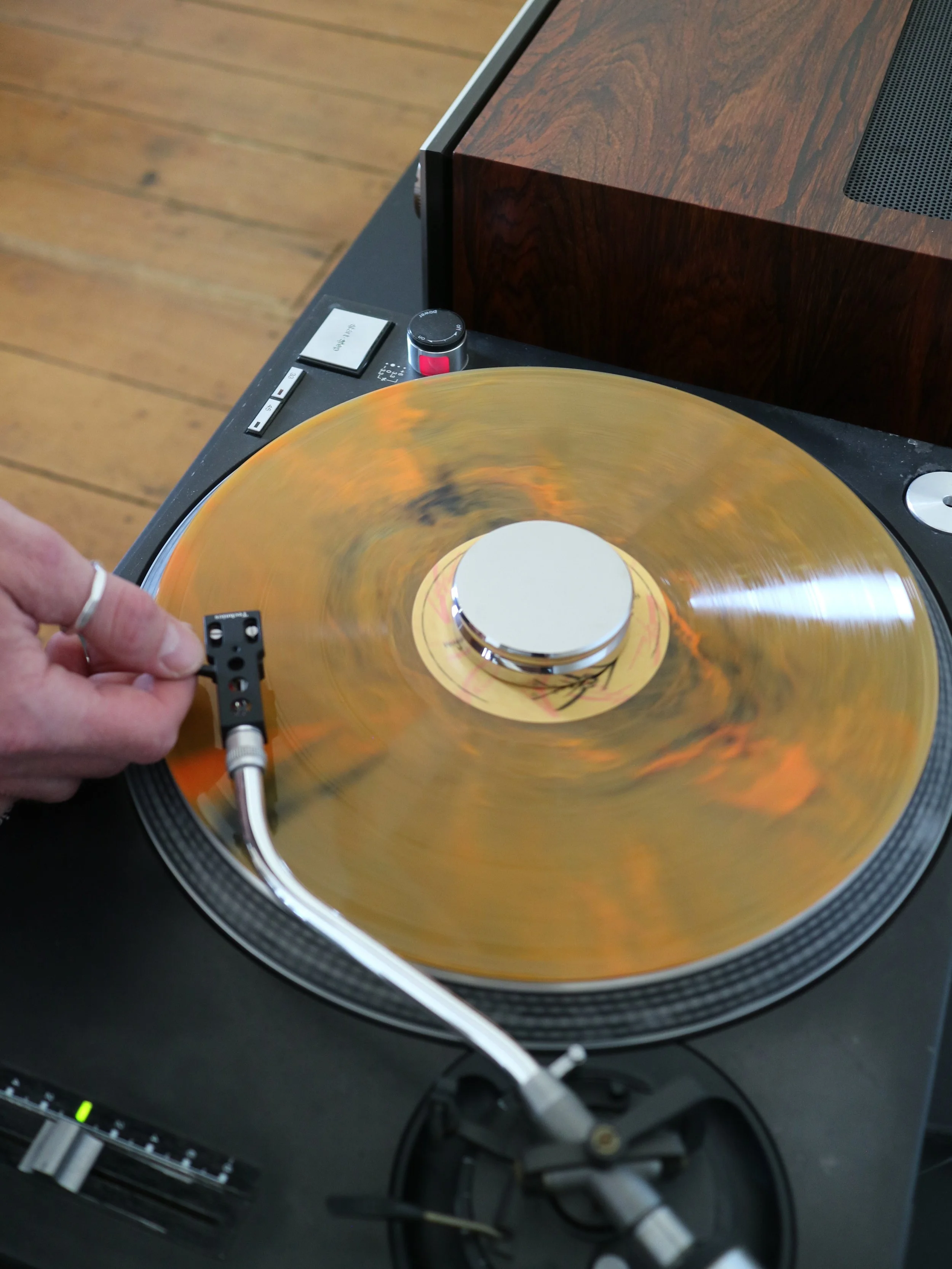 Close-up of a turntable playing a vinyl record with a wooden speaker nearby.