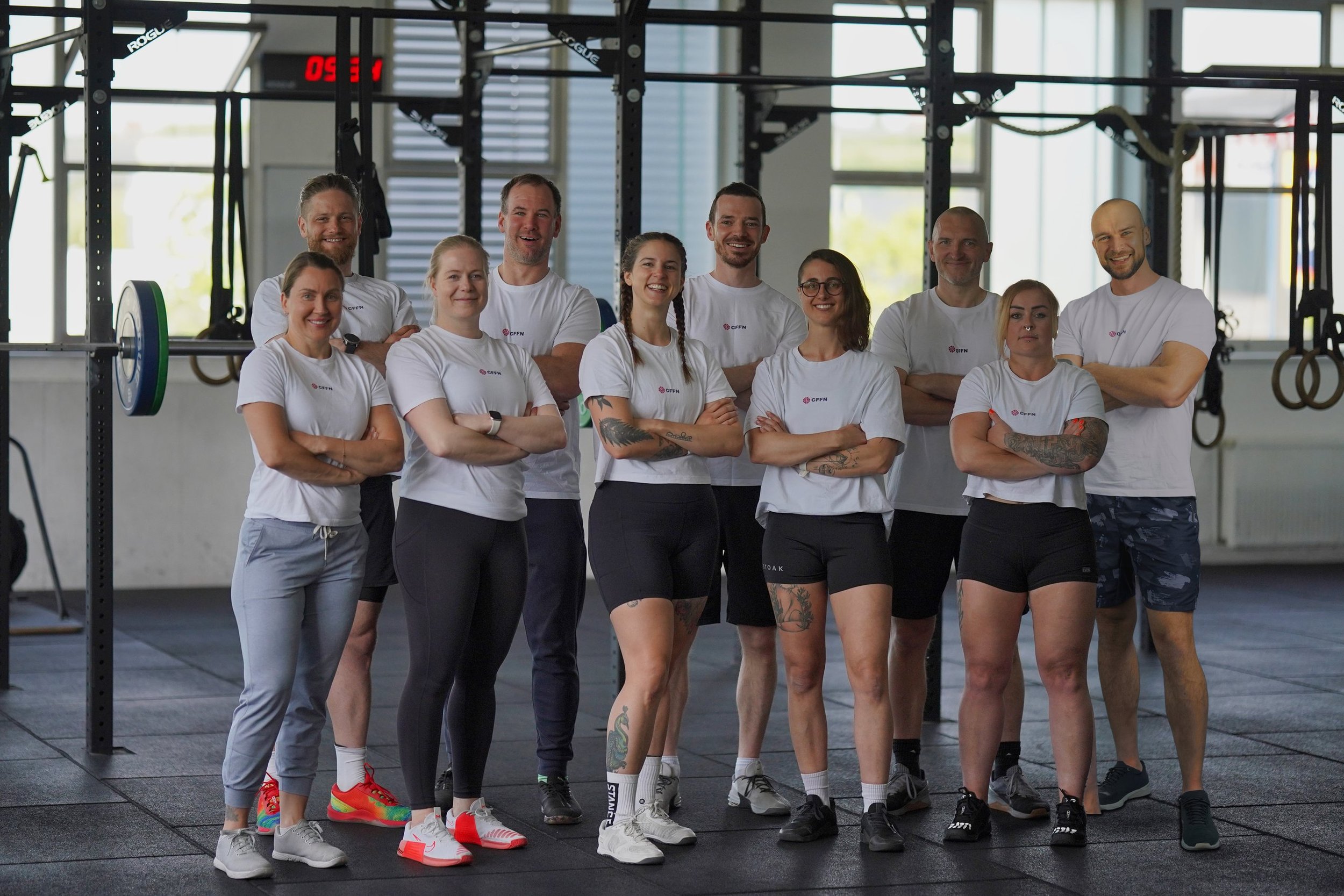 Das Coach-Team von CrossFit Friedrichshafen: zehn Coaches in weißen CFFN-Shirts mit verschränkten Armen in der Box