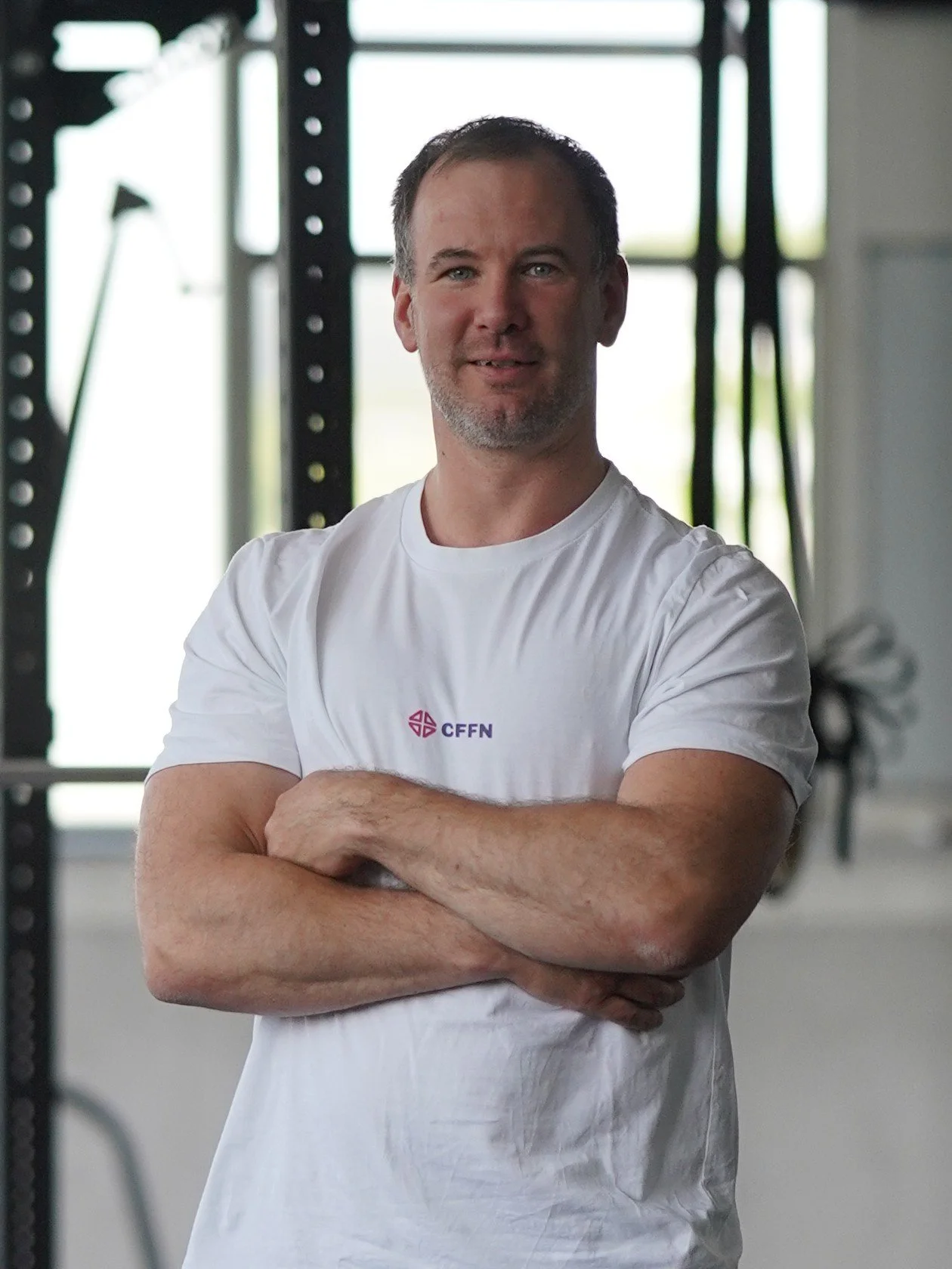 Andi, Coach bei CrossFit Friedrichshafen, im weißen CFFN-Shirt mit verschränkten Armen in der Box