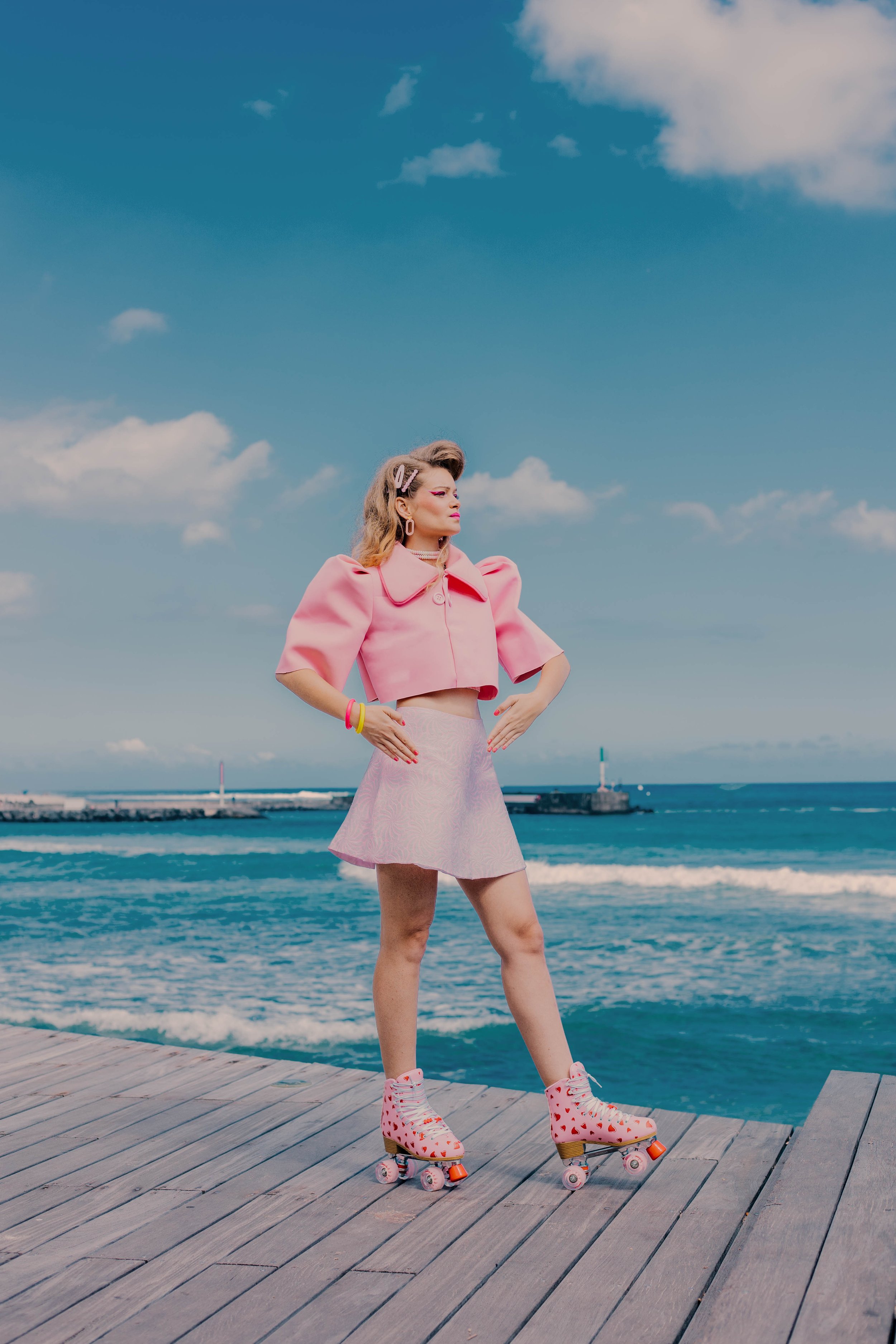 Une femme en vêtements roses et roller en position statique sur un quai en bois au bord de la mer.