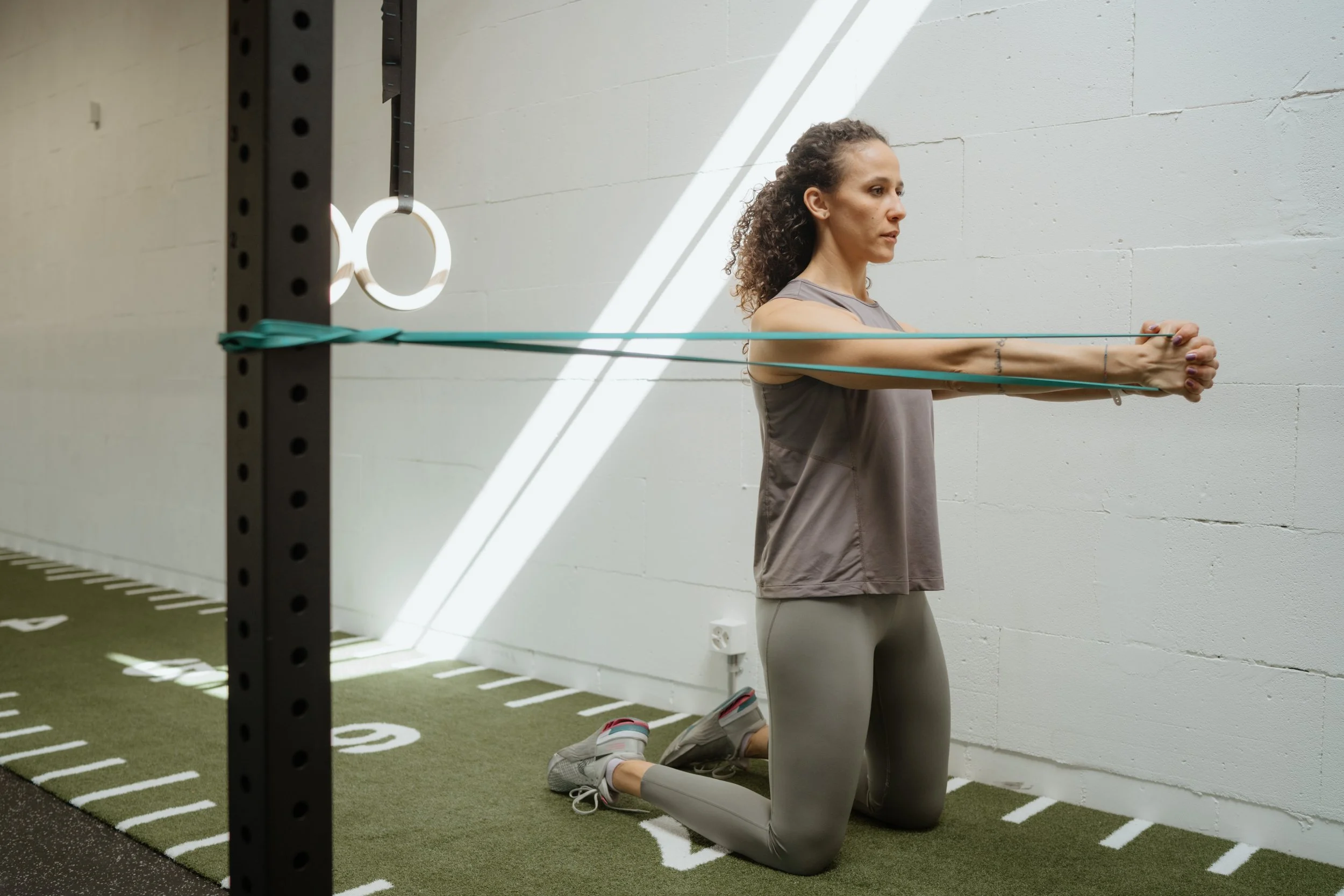 Frau beim Krafttraining mit Widerstandsbändern, kniend auf einer Turnmatte in einem Fitnessstudio.