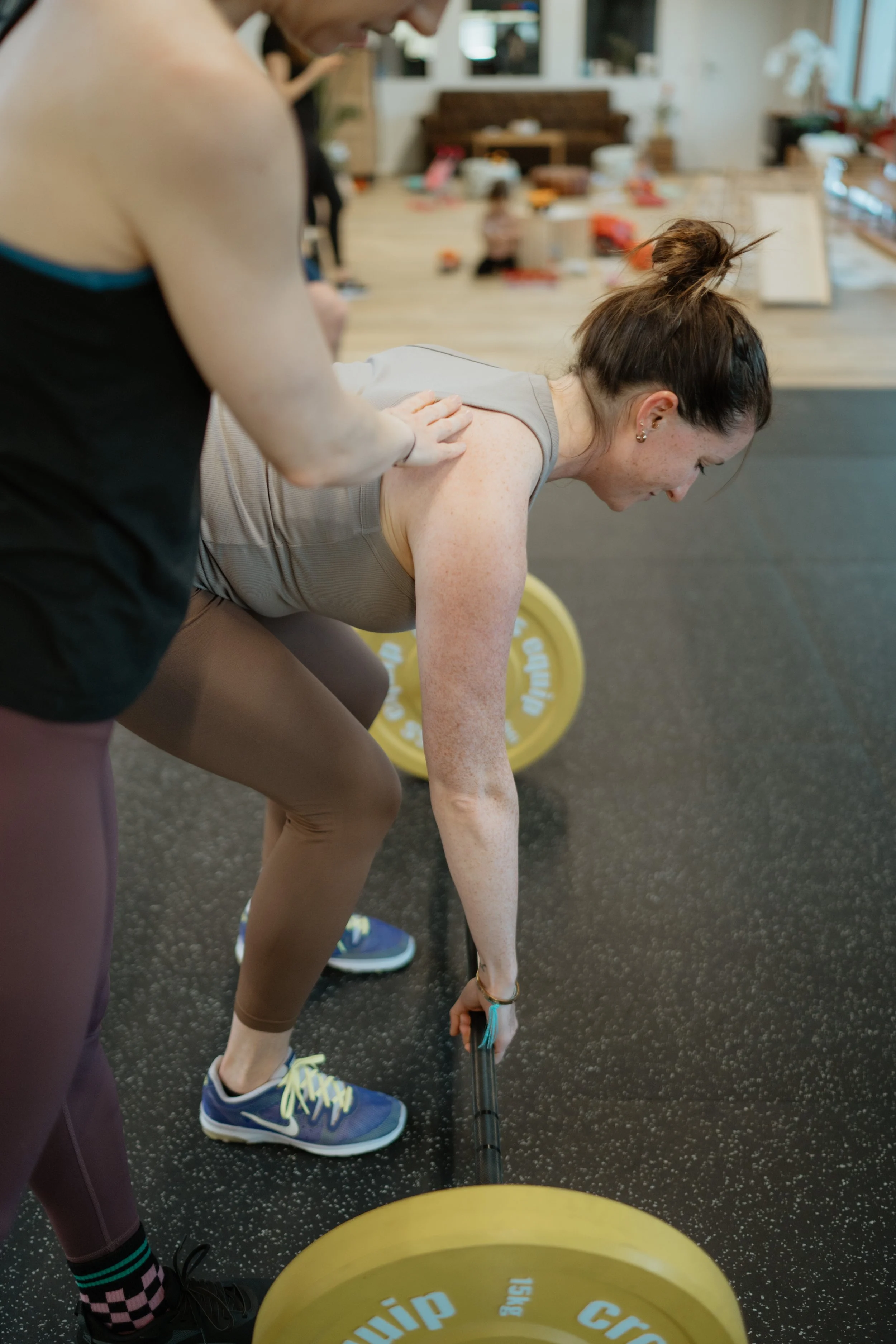 Eine Frau hebt eine Hantel im Fitnessstudio, während sie von einer Trainerin unterstützt wird.