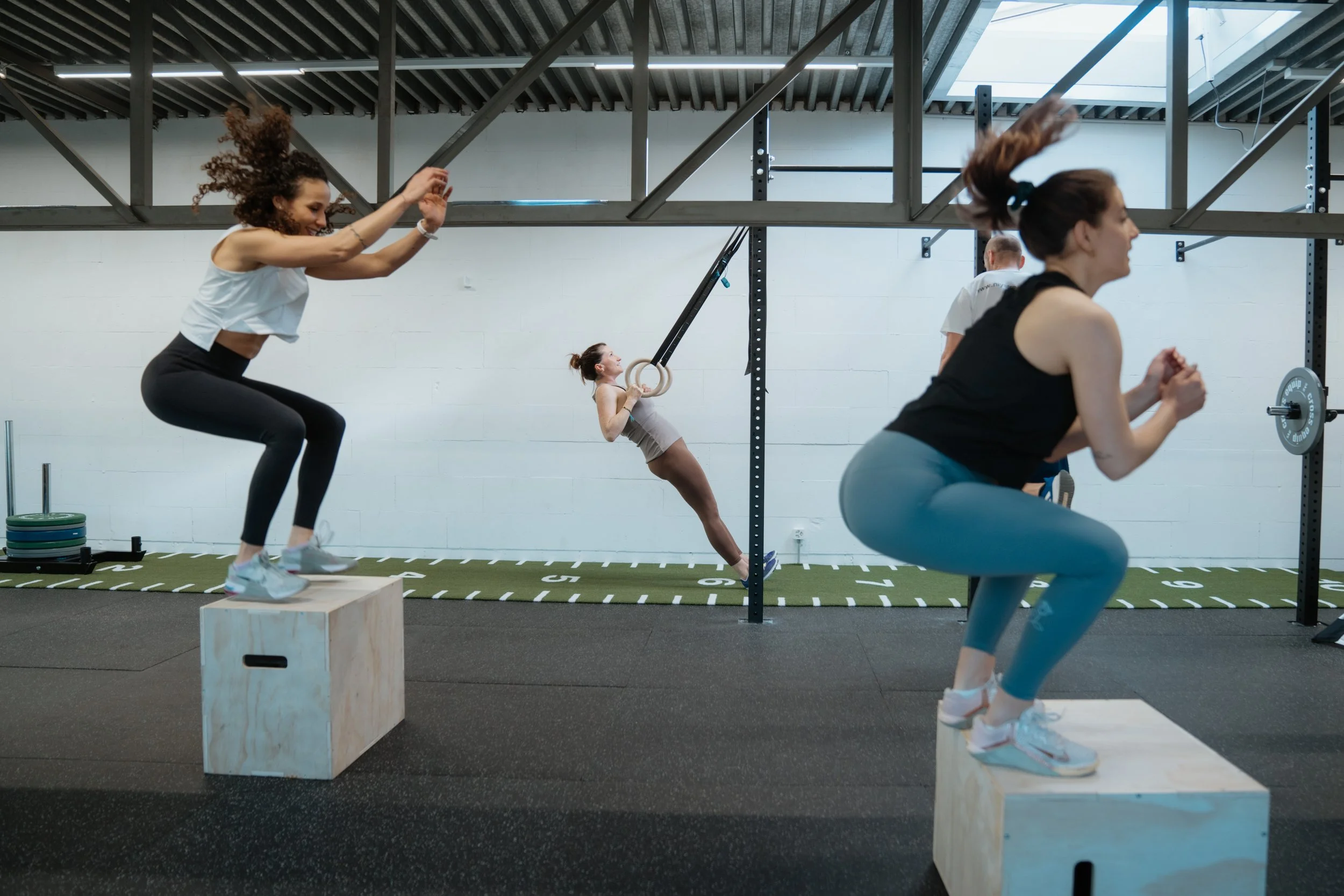 Menschen trainieren in einer Fitnessstudio mit plyometrischen Kisten, Gymnastikringen und Kraftgeräten.