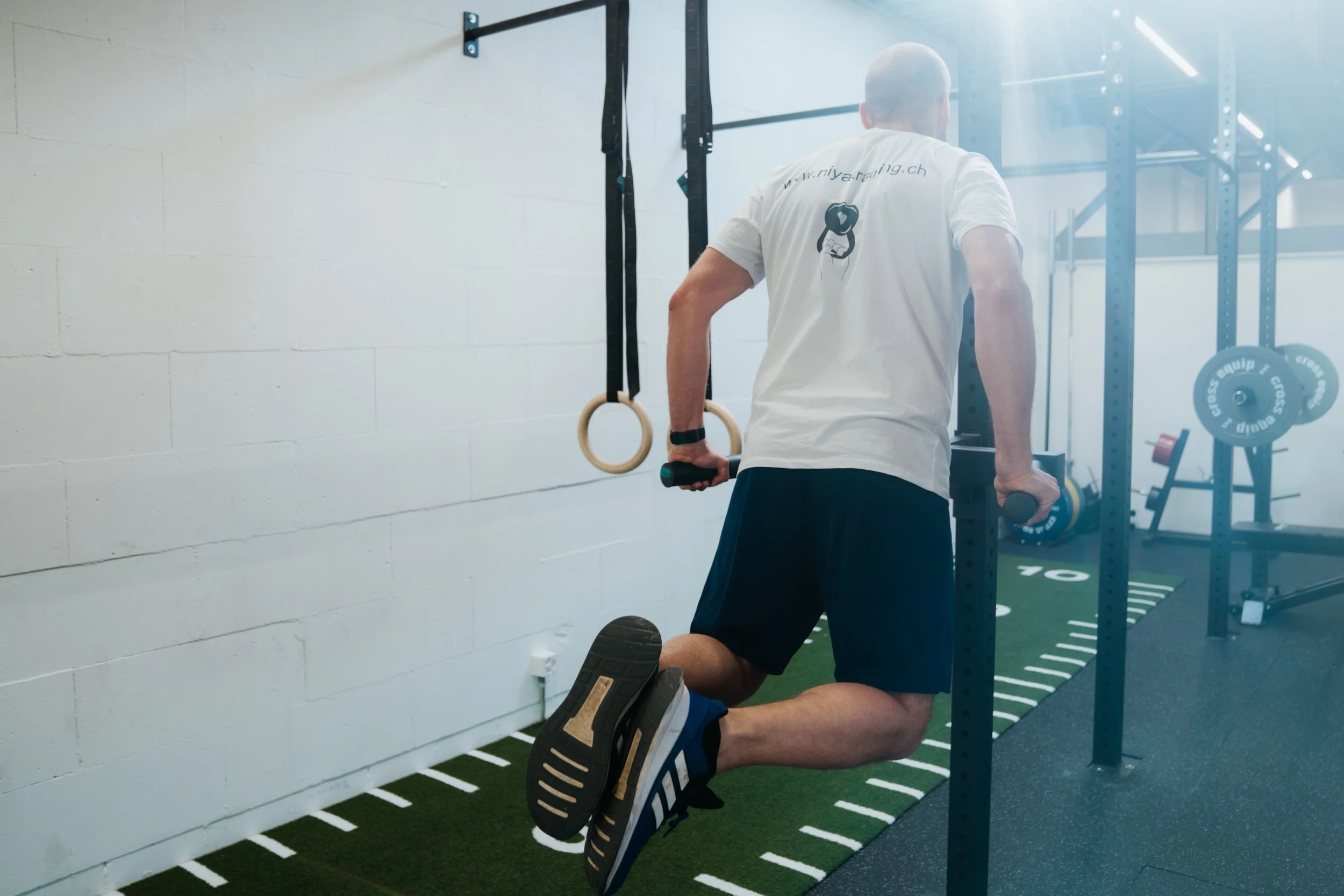 Ein Mann trainiert im Fitnessstudio, macht Liegestütze auf einer Hackenbank, trägt ein weißes T-Shirt und schwarze Shorts.