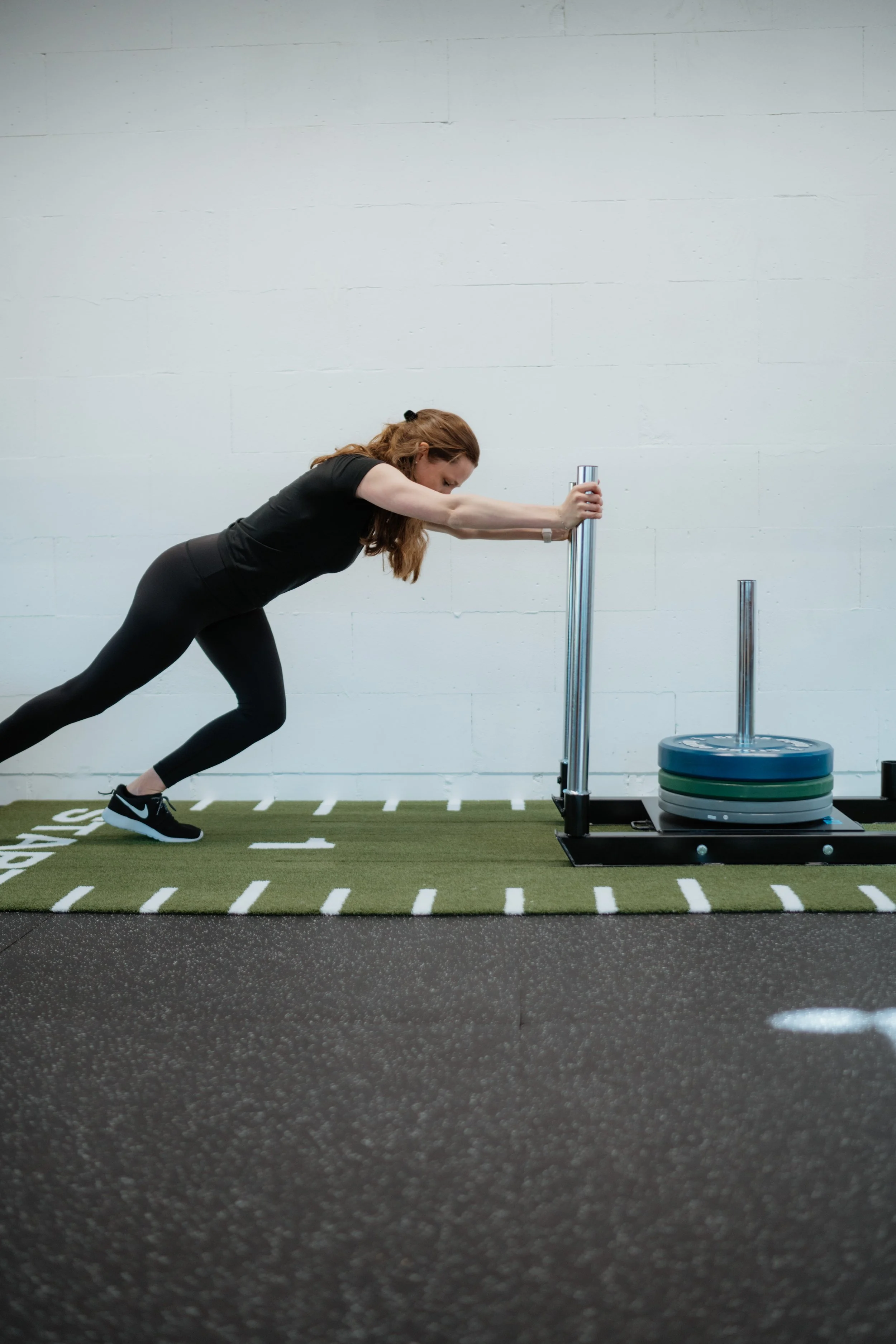 Eine Frau beim Push-Plate-Training im Fitnessstudio, die sich nach vorne lehnt und die Stange nach unten drückt.