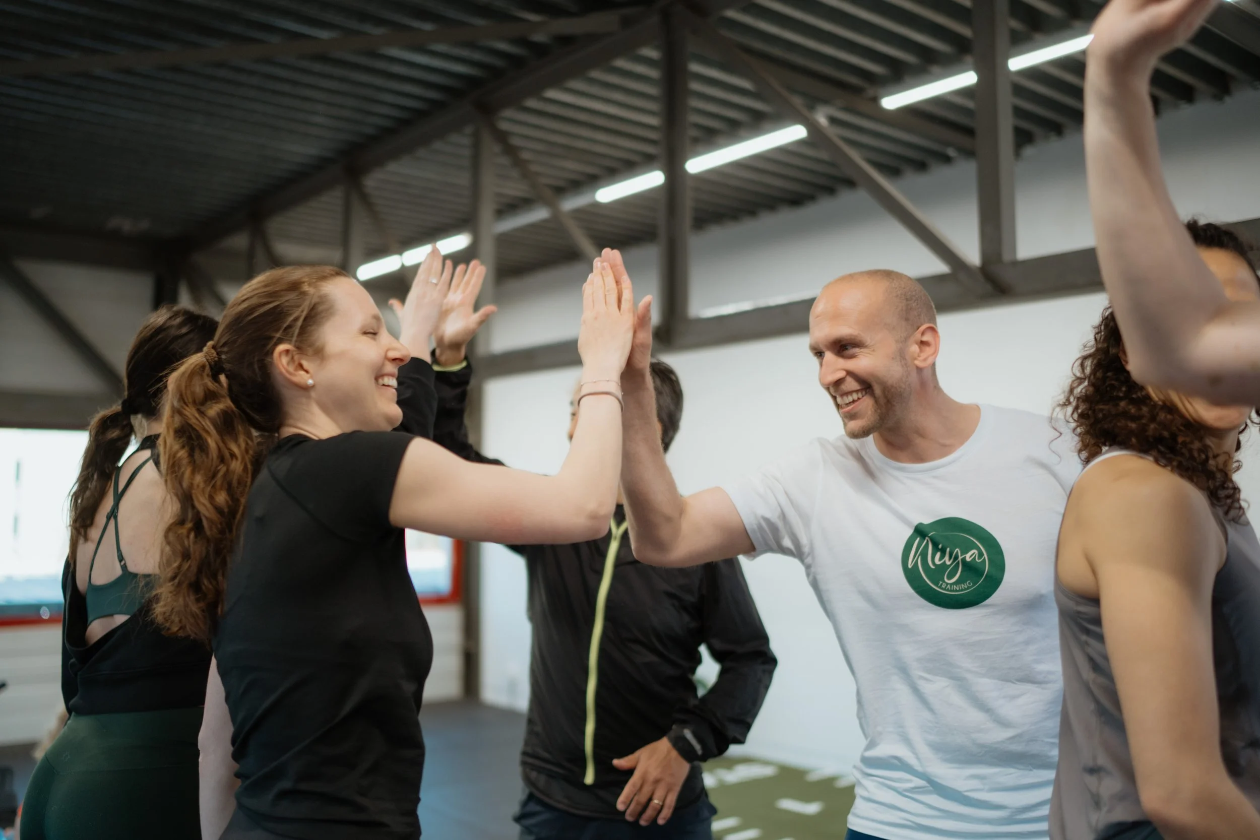 Zwei Menschen feiern ein High-Five in einem Fitnessstudio, lachend und umgeben von weiteren Personen, mit sportlicher Kleidung.