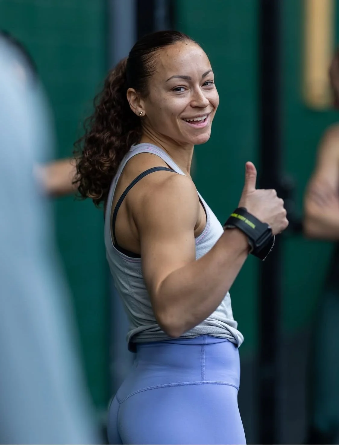 Frau in Sportkleidung, die im Fitnessstudio ein Daumen-hoch-Geste macht und lächelt.