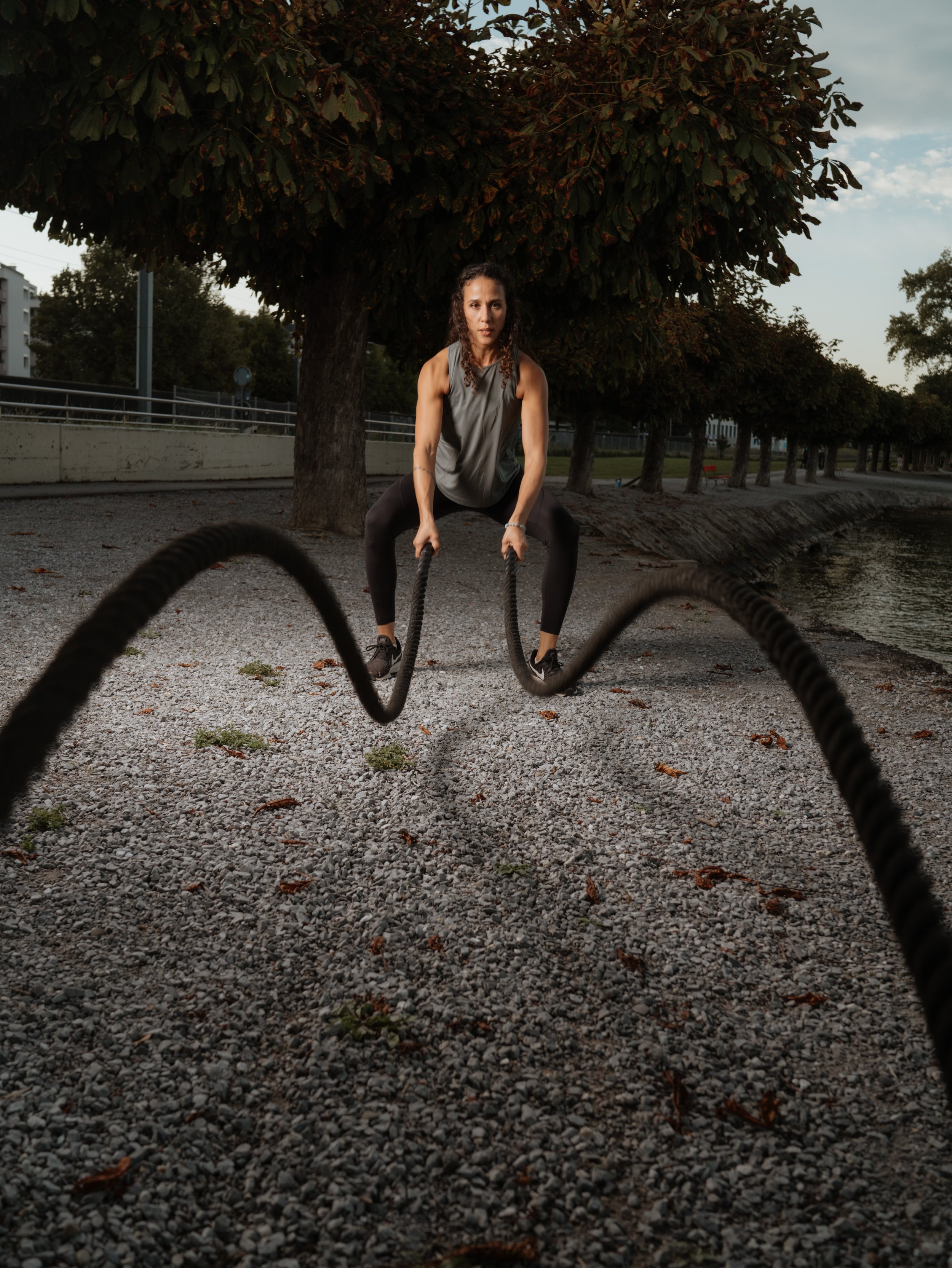 Frau beim Training mit Seilklettern im Freien an einem Nachmittag, Bäume und Wasser im Hintergrund.