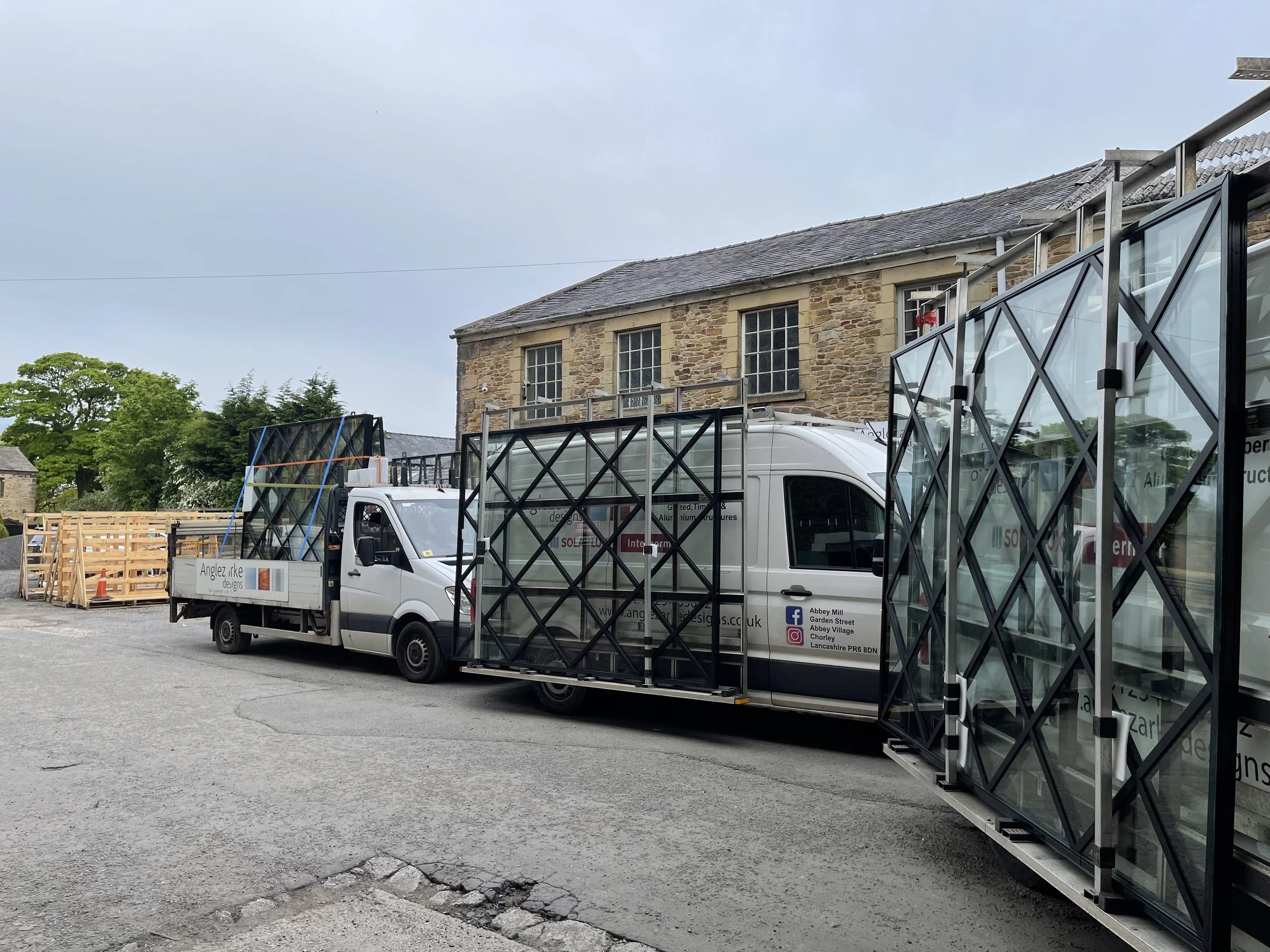 Delivery truck parked beside a stone building with glass window panels and wooden crates in the background.