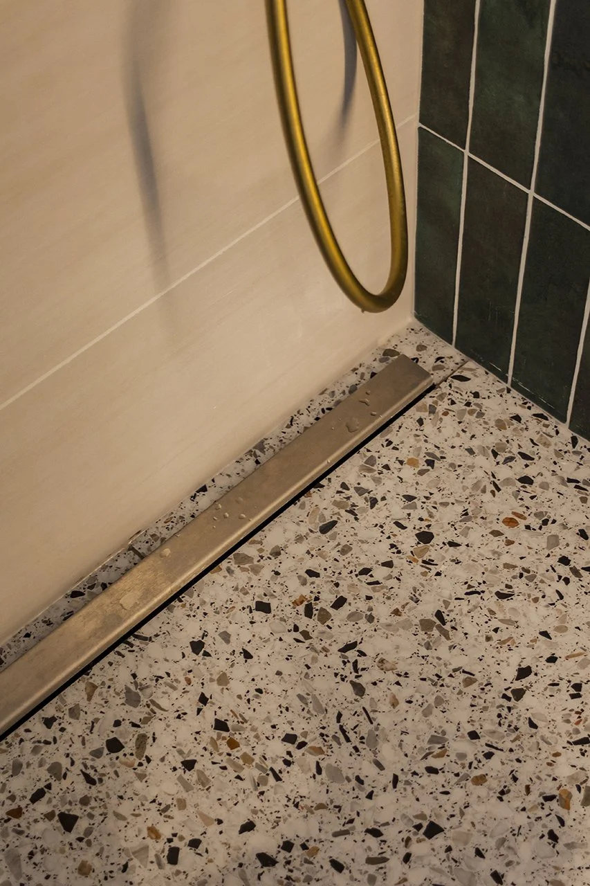 détail du sol de la douche avec le carrelage effet terrazzo et la bonde en métal