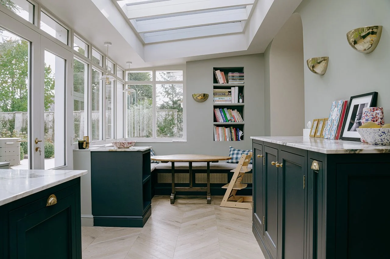 Une cuisine classique moulurée avec un parquet point de hongrie et une verrière donnant sur le jardin. Un espace repas familial est créer dans un angle, entouré de banquettes