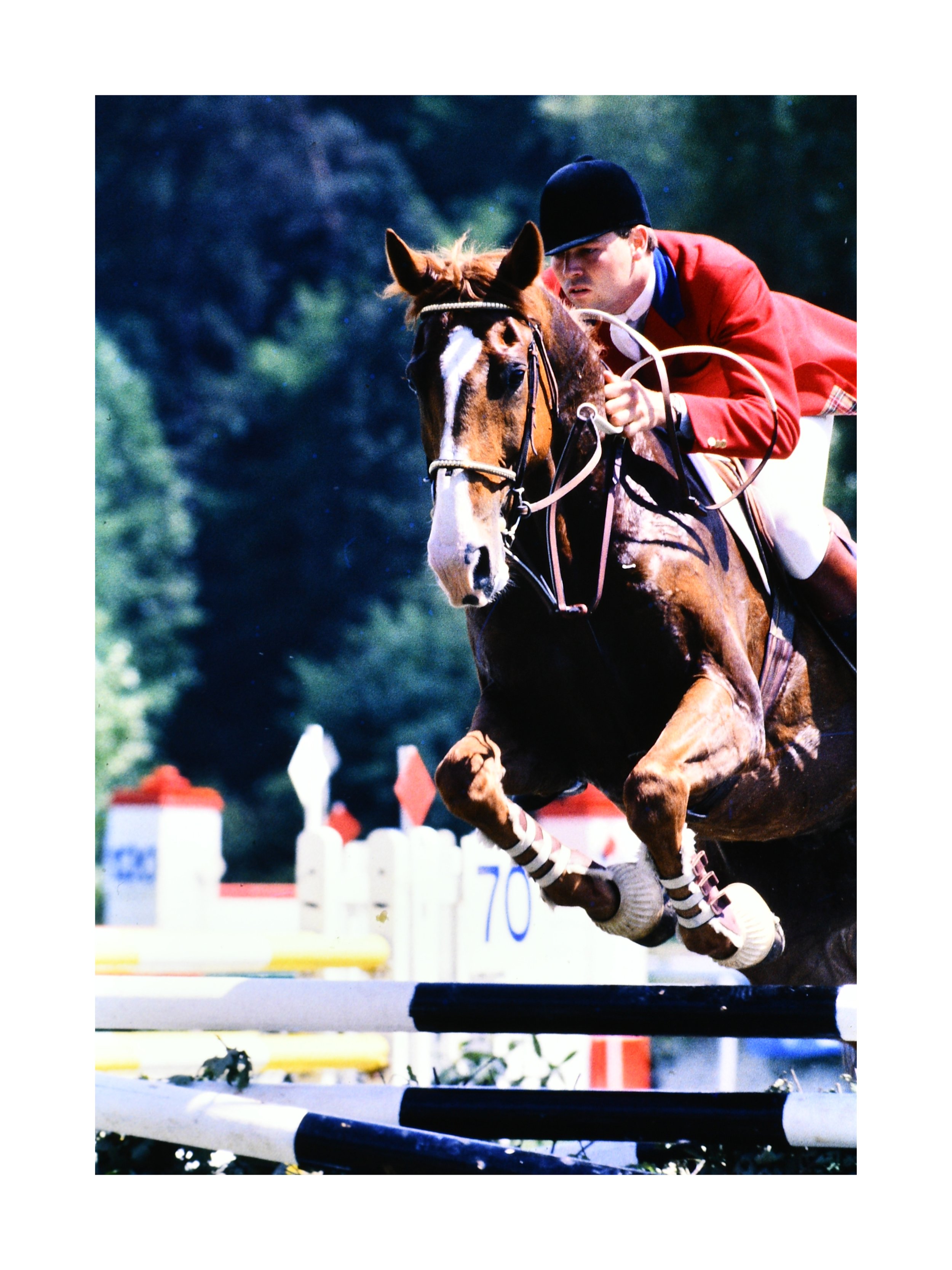 Photographie argentique d’un saut d’obstacle lors d’un concours hippique en 1985, cavalier en veste rouge franchissant une barre, archive de Didier Arrès.