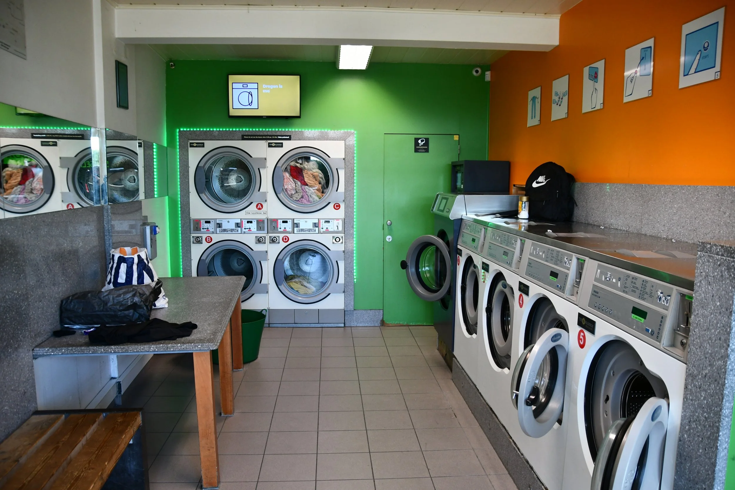 Luchtvaartaansicht van een wasserette met meerdere wasmachines en drogers, een tafel, een bank en een groene muur.