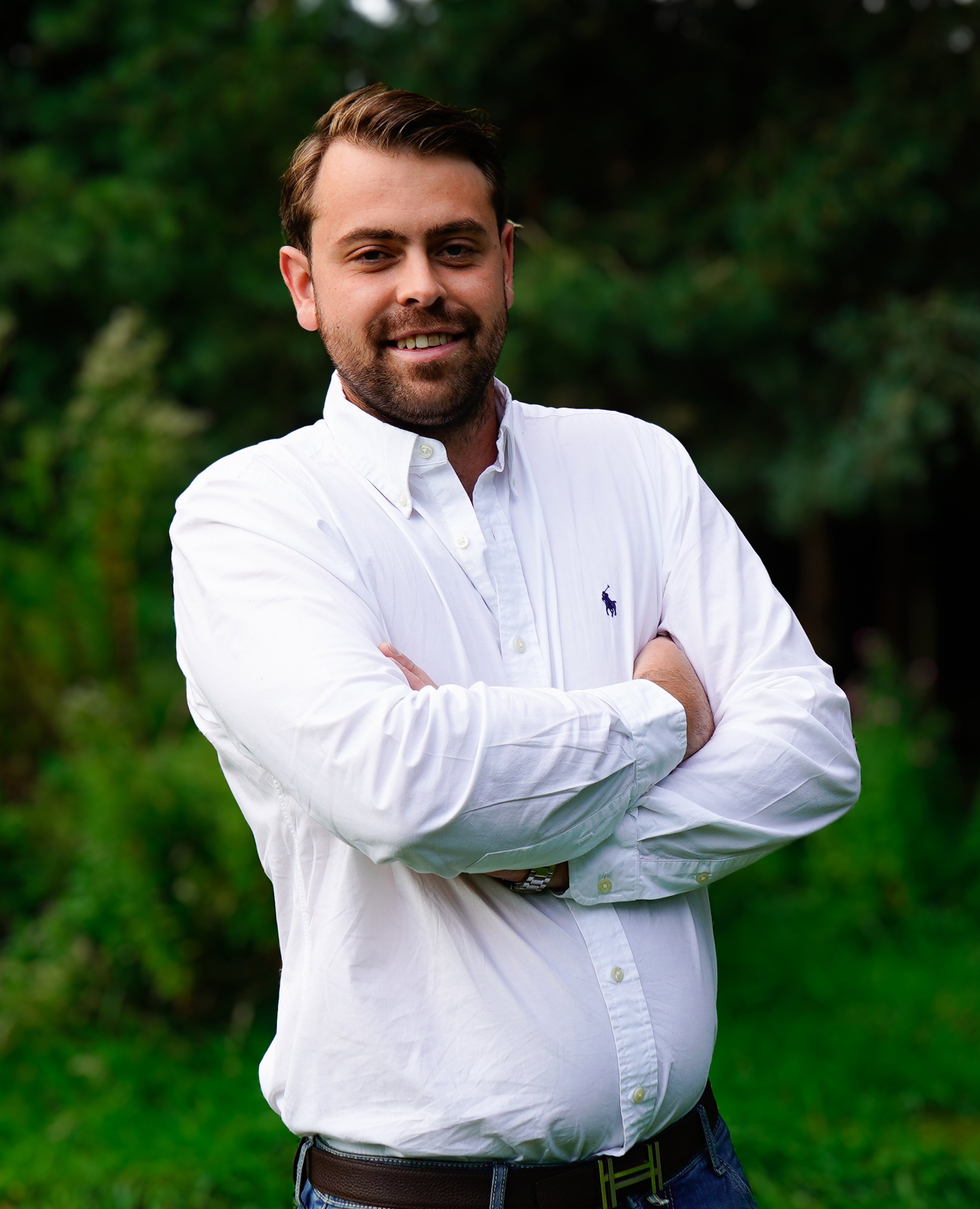 man lacht, met armen gekruist, in een witte blouse, buiten groene achtergrond