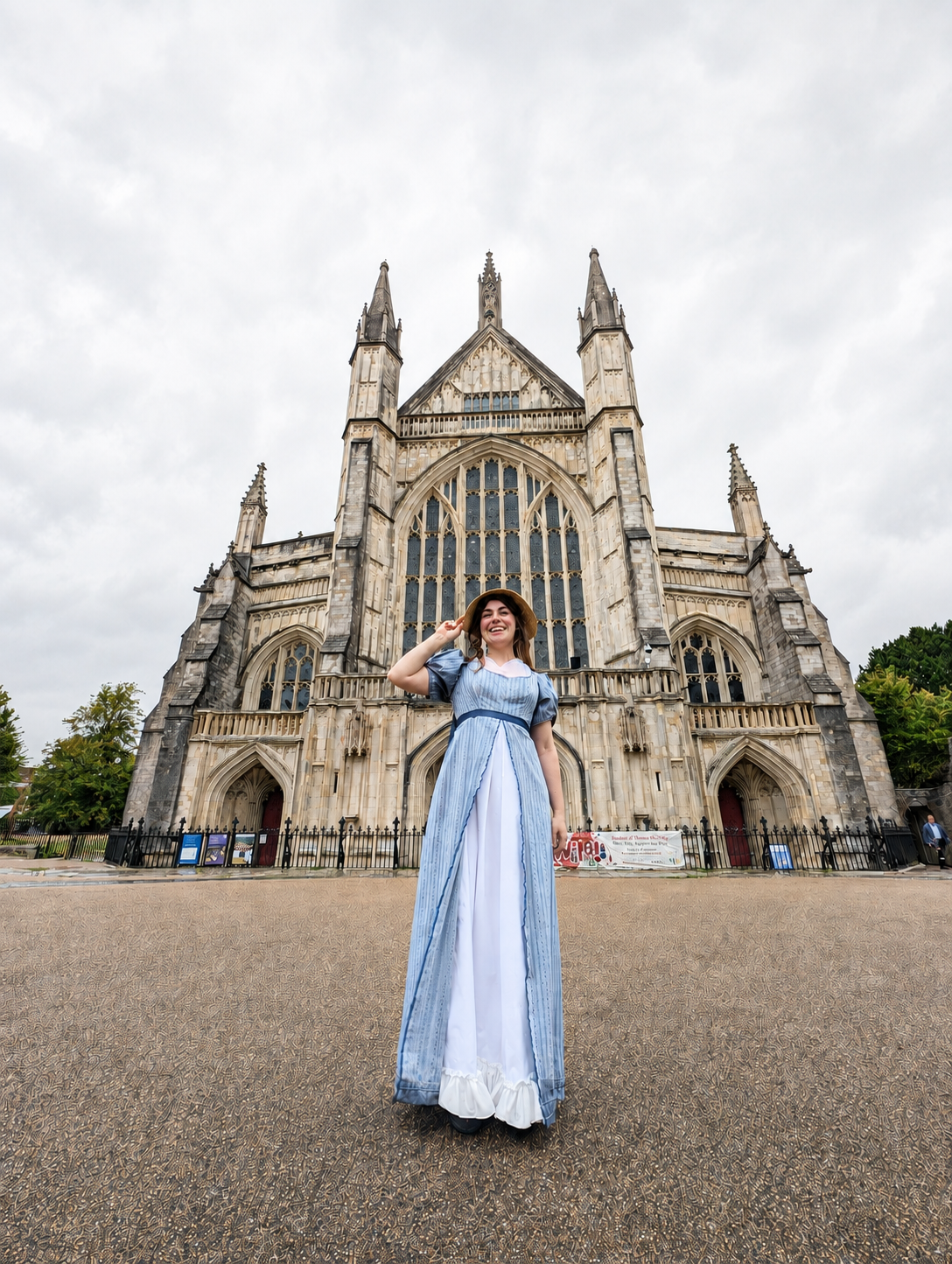 Woman in historical dress smiling in front of a large Gothic cathedral with pointed arches and tall spires.