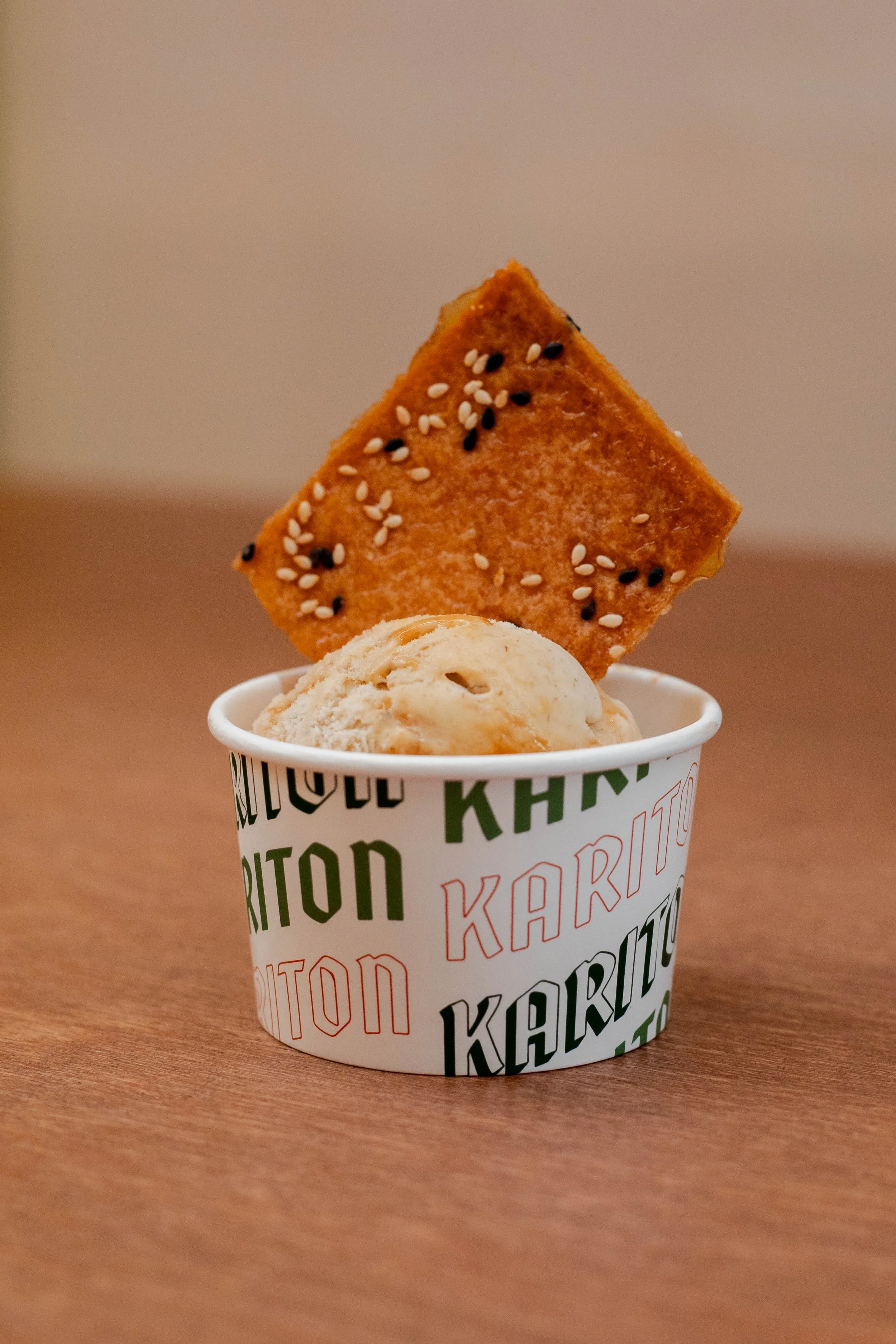 A cup of vanilla ice cream with a sesame seed and black sesame seed cracker on top.