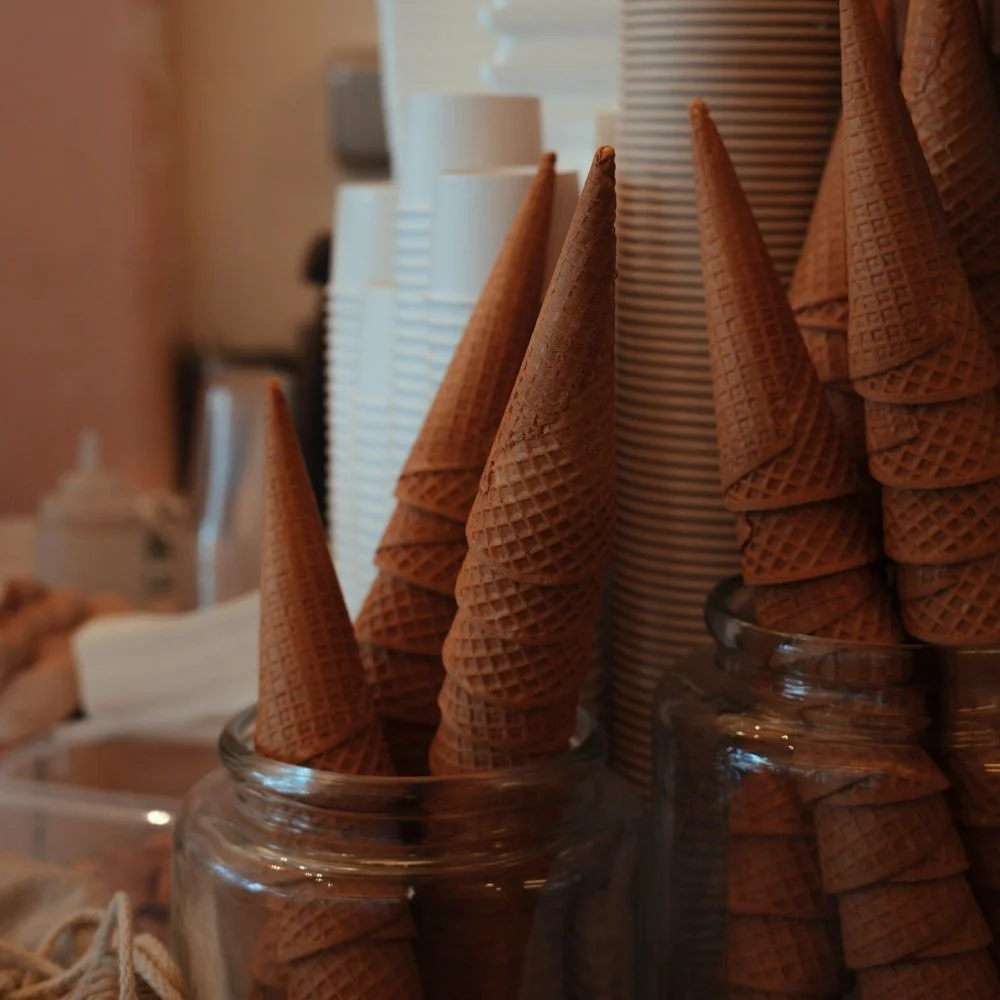 Stacked empty waffle cones in glass jars, with some disposable cups and a water bottle in the background.