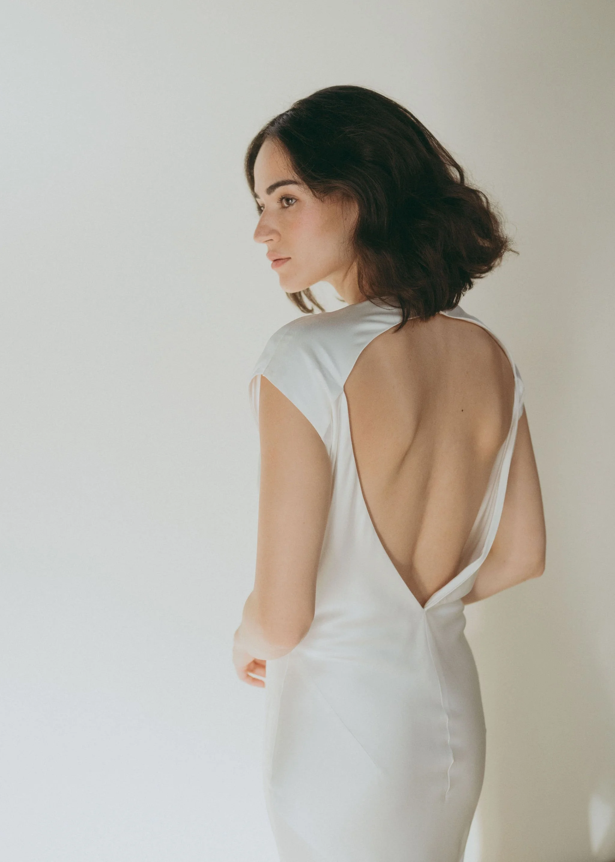 Beatrice Dress by Rolling in Roses – minimalist satin bridal gown with high cowl neckline, open back, angular darts, and detachable wrist loop, crafted from sustainable vegan satin and organic bamboo, available at Lyra Bridal Studio, UK
