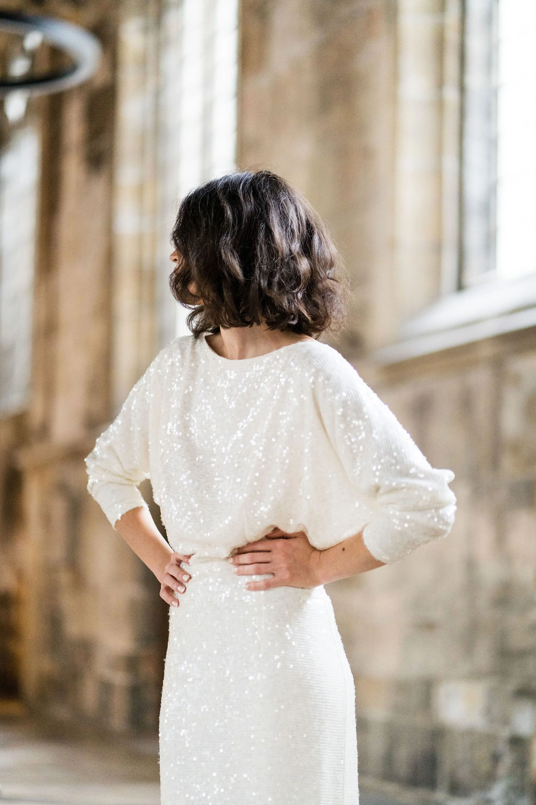 Ophelia Dress by Rolling in Roses – shimmering georgette bridal gown fully embroidered with subtle sequins, featuring a high neckline, plunging open back, fitted skirt with petite godet, and modest train. Includes optional ribbon tie for added securi